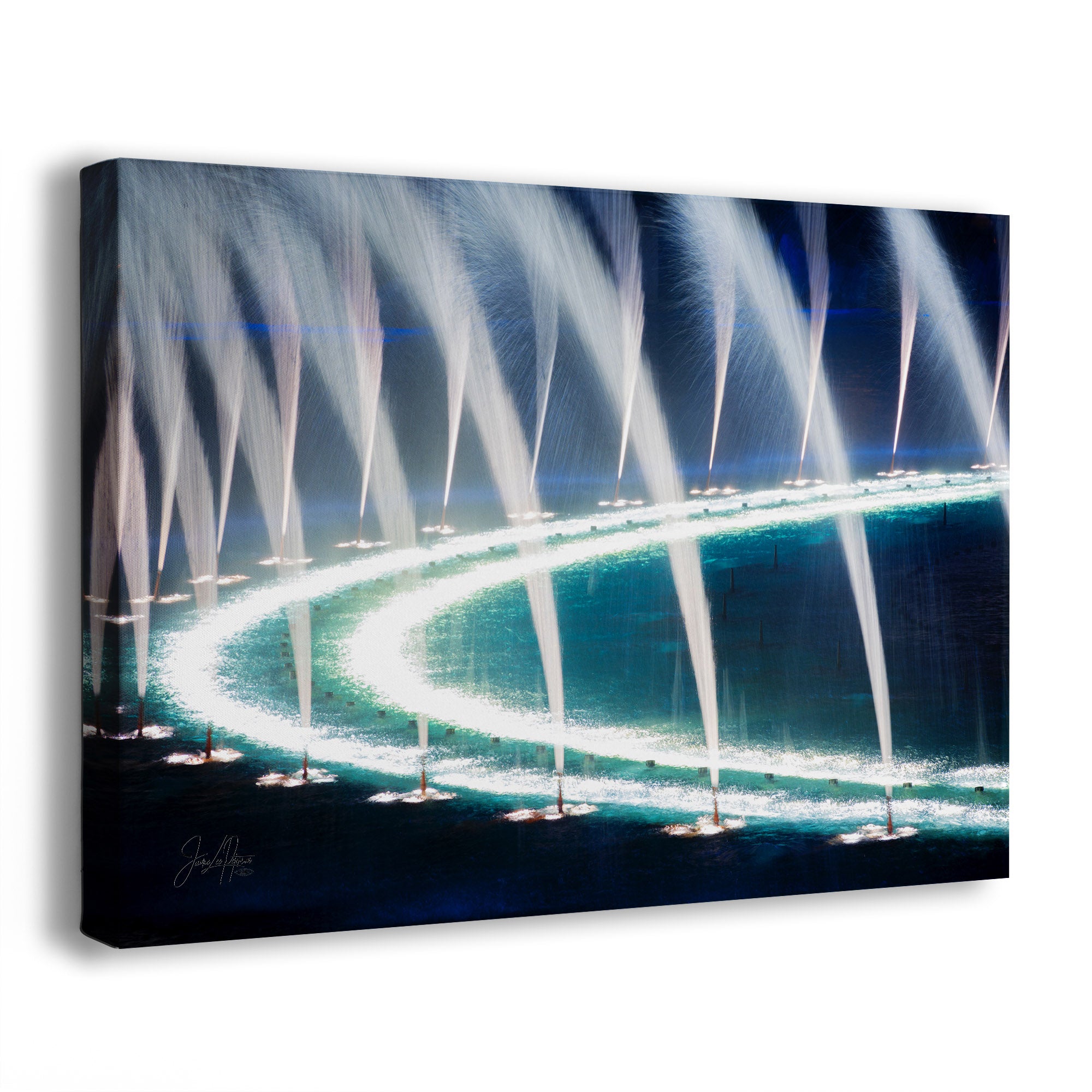 A rectangular wall art print or canvas showing a nighttime fountain display with bright white water jets curving over a dark blue and black base. The artwork is photographed at a slight angle against a clean white background.