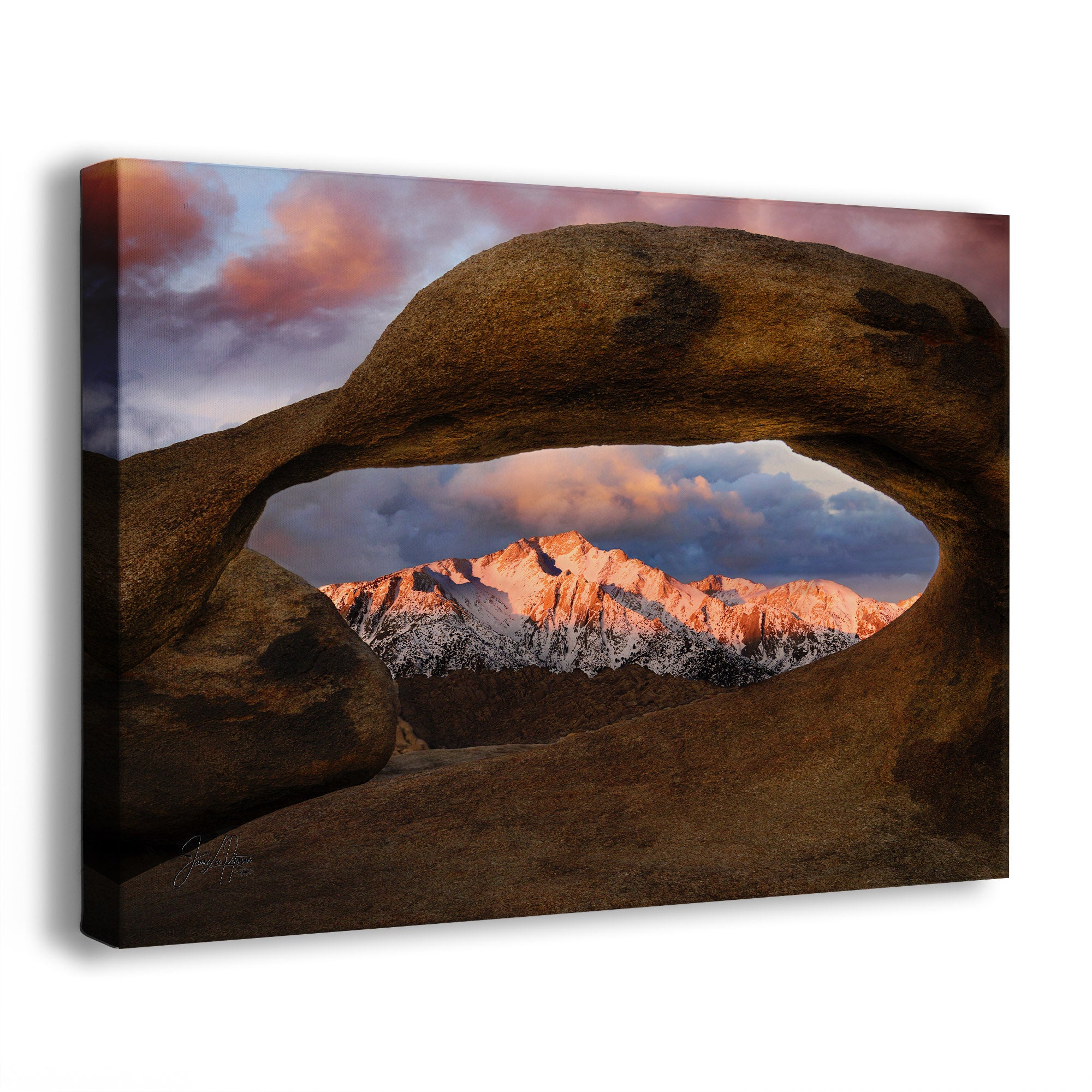 A canvas wall art print looking through Mobius Arch at the Alabama Hills at Lone Pine Peak of the Sierra Nevada mountains. It's a natural desert arch with snow-capped mountains and a colorful sunrise sky. 