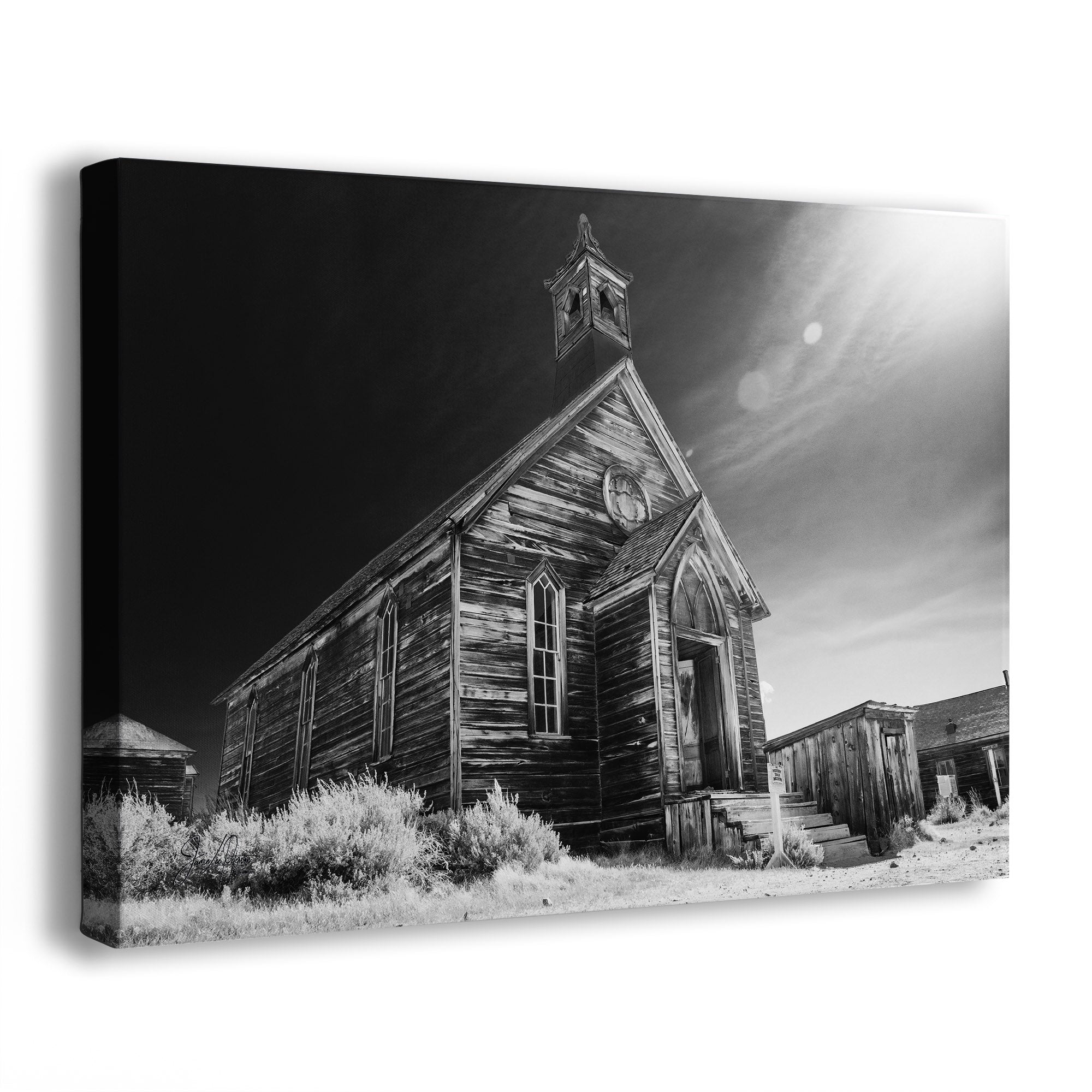 Black and white canvas wall art featuring an old wooden church in Bodie Ghost Town in a desert landscape, shown as a gallery-wrapped canvas at an angle against a white background.