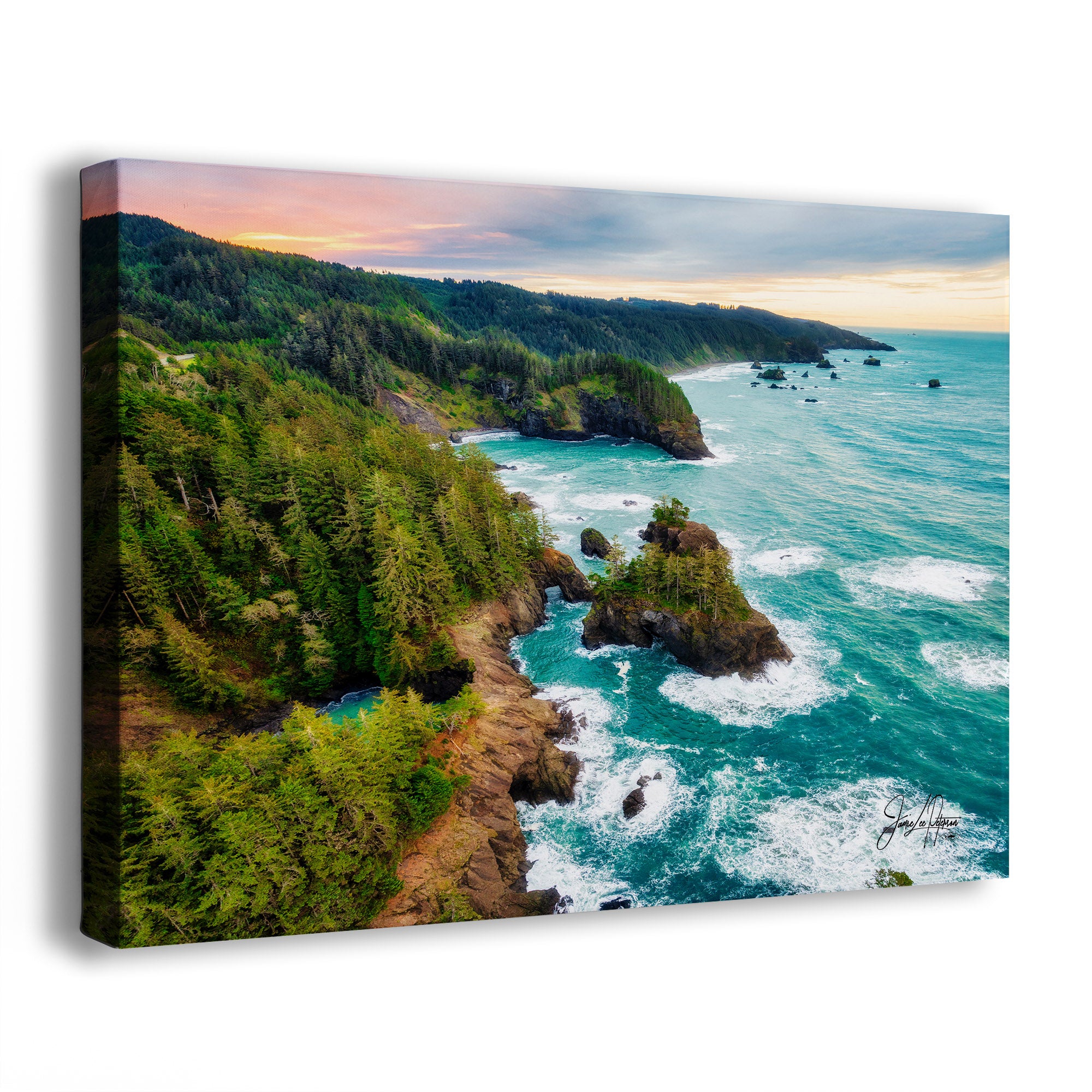 A canvas wall art print showing an aerial coastal landscape with dense green forested cliffs, rocky shoreline, turquoise ocean water, and a cloudy sunset sky. The canvas is photographed at an angle against a plain white background.