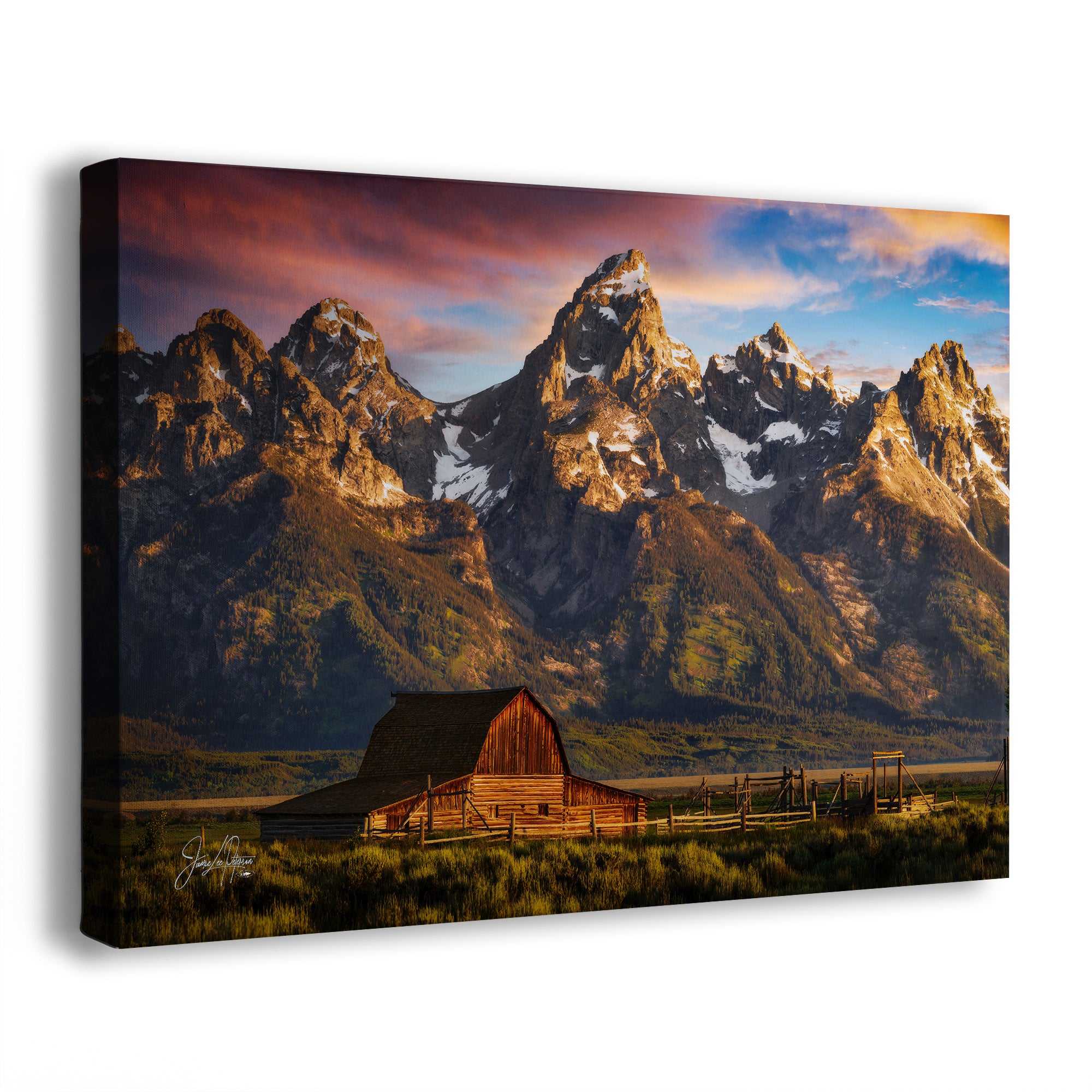 A rectangular canvas wall art print showing the Grand Teton mountain landscape at sunrise, with snow-capped peaks, the wooden Moulton Barn in the foreground, and a fence line. The canvas is photographed at a slight angle on a clean white background.