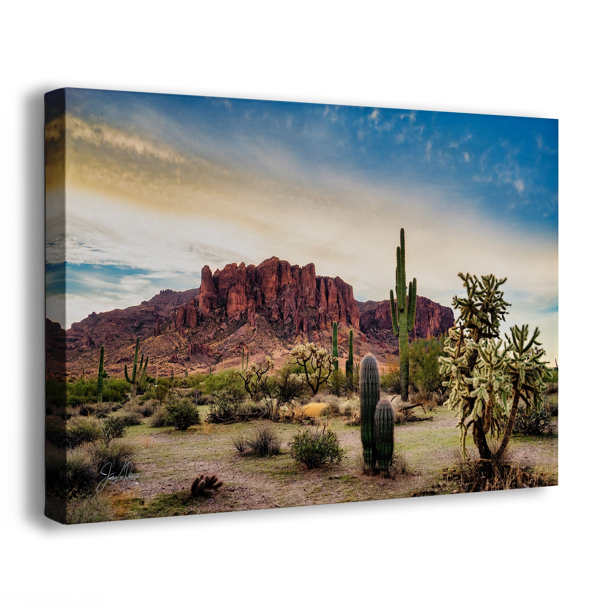 A canvas wall art print showing a desert landscape of the Superstition Mountains at Lost Dutchman State Park with red rock mountains, saguaro cacti, cholla plants, and a blue sky with warm clouds, photographed against a plain white background.
