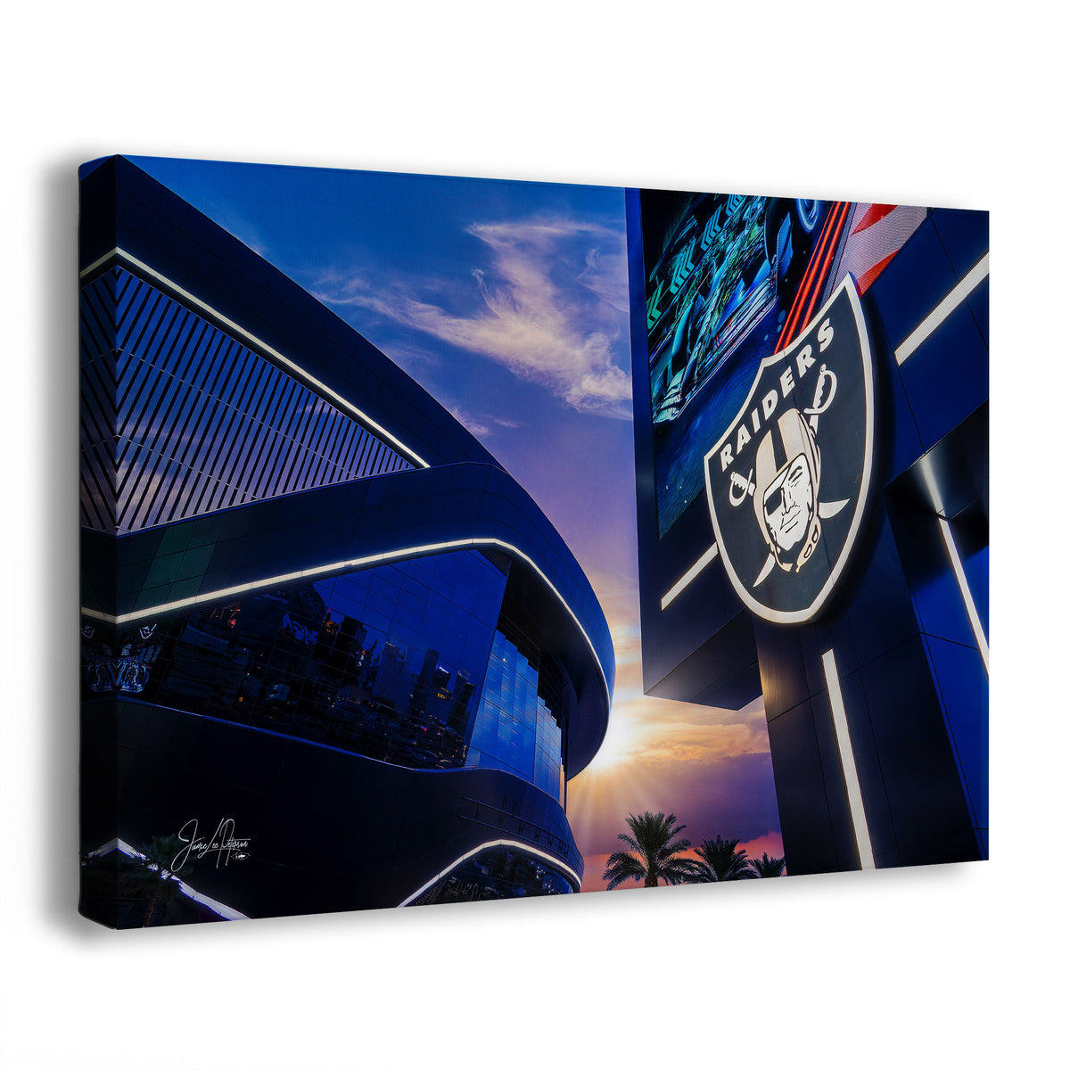A wall art print or canvas showing a dramatic low-angle photograph of the Las Vegas Raiders stadium at sunset, with a large Raiders logo visible on the right and blue sky and reflective architecture across the scene.