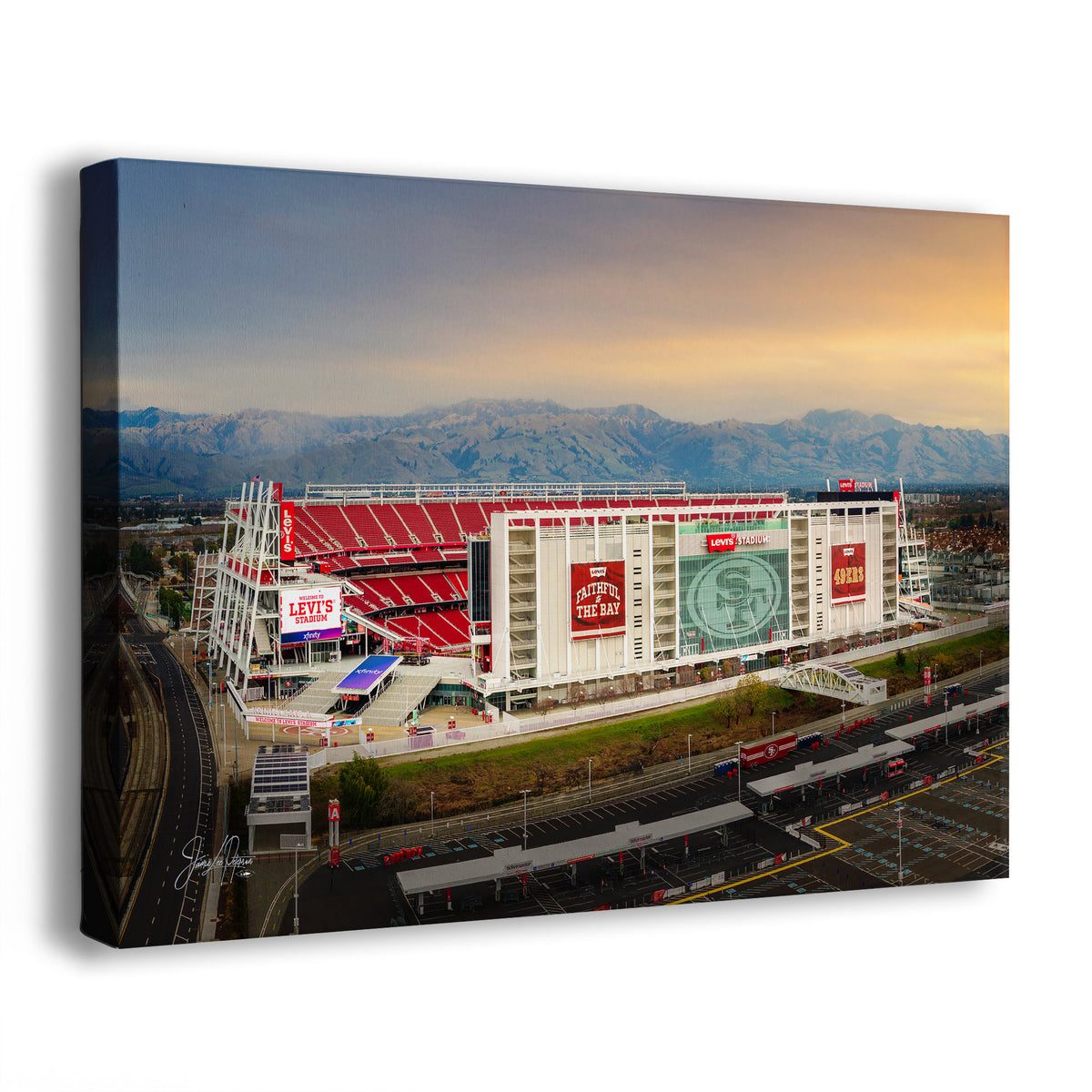 A San Francisco 49ers Stadium Art print showing an aerial view of a large stadium with red seating, mountain ranges in the background, roads, and parking structures. The print is photographed at an angle against a plain white background.