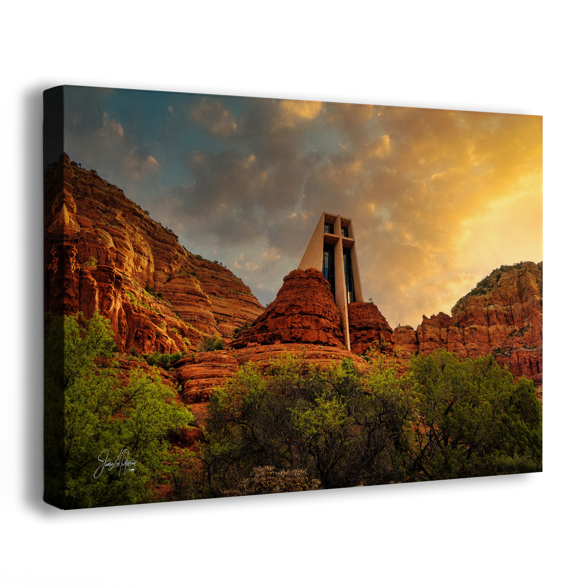 A rectangular canvas wall art print showing the Sedona, Arizona, desert landscape with the Chapel of the Holy Cross, red rock cliffs, green trees in the foreground, and a dramatic golden sky. The canvas is photographed at an angle against a plain white background, with the left side showing a dark wrapped edge.