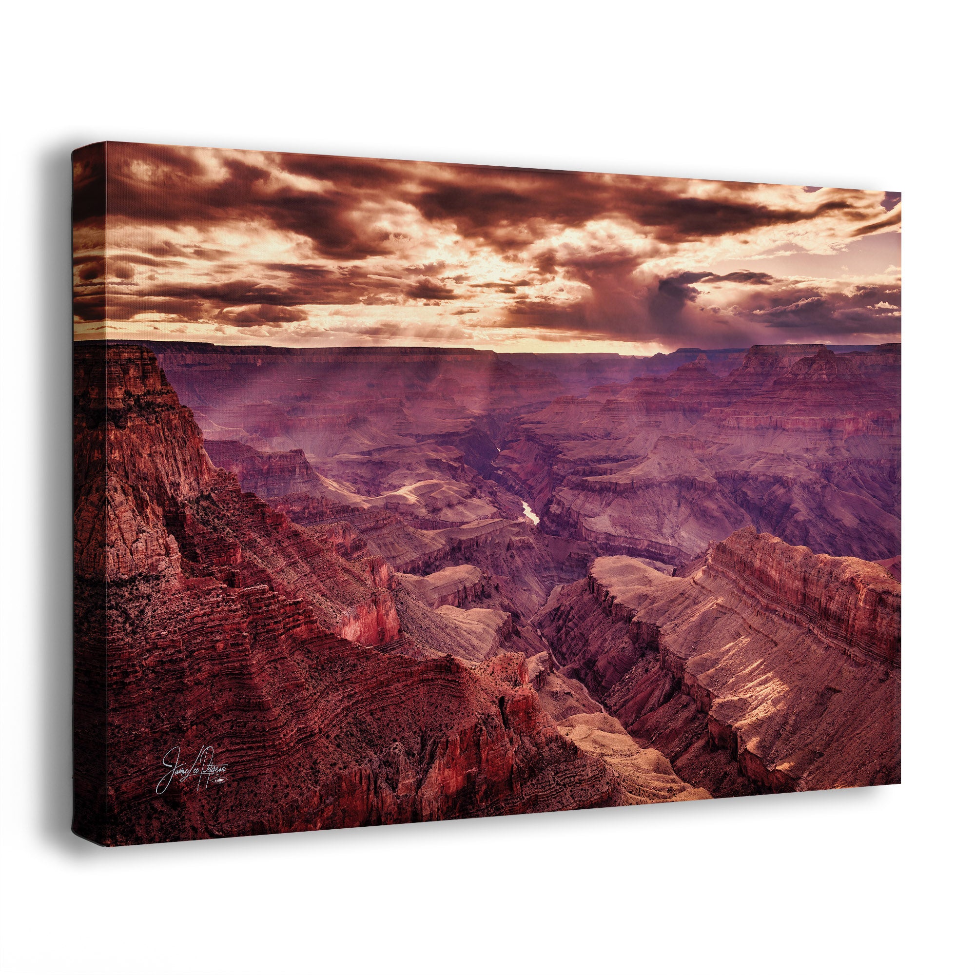 A canvas wall art print showing a dramatic Grand Canyon landscape at sunset, photographed at an angle against a plain white background. The artwork depicts layered red, purple, and brown rock formations under a cloudy sky with warm golden light.
