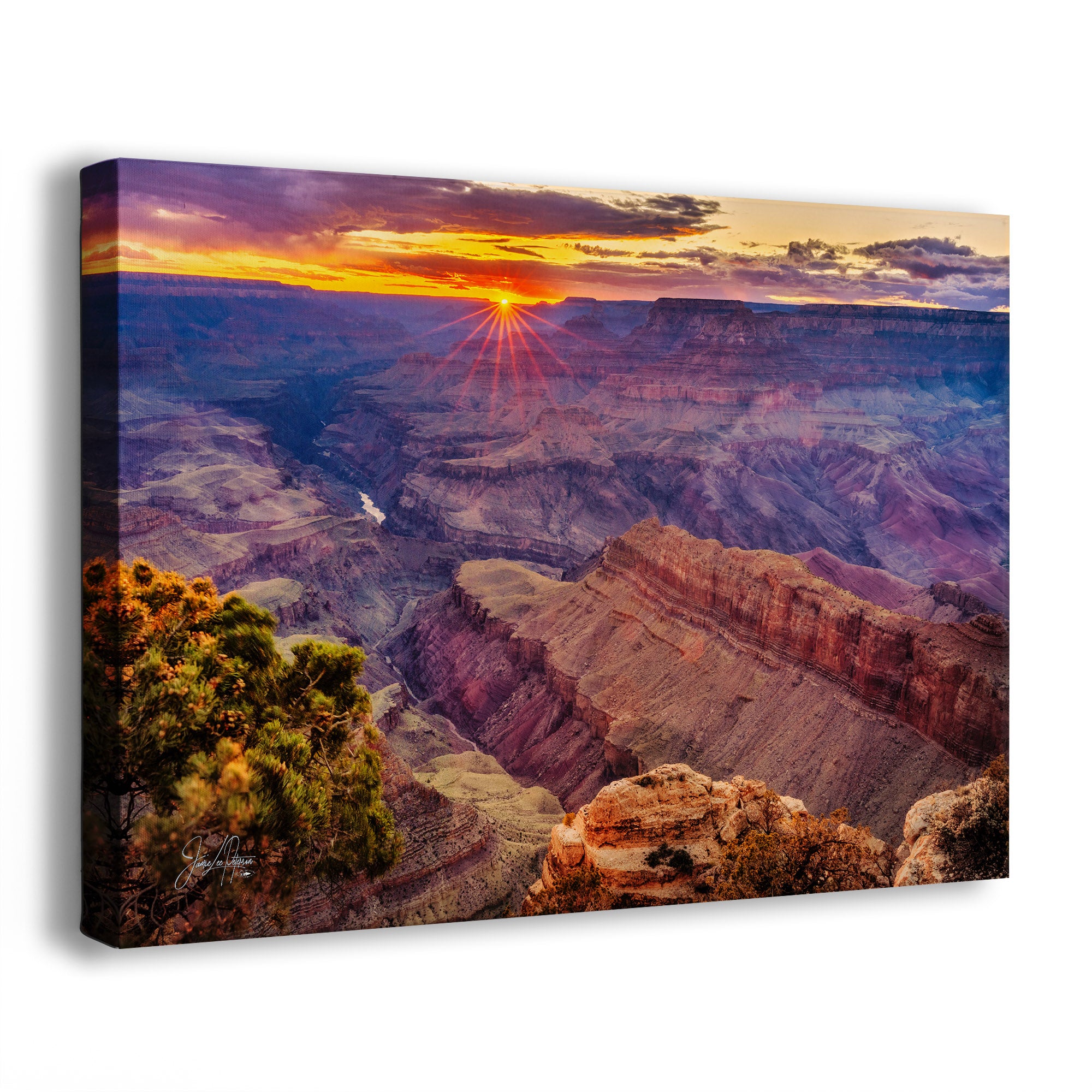 A rectangular canvas wall art print showing a dramatic sunset over the Grand Canyon, photographed at an angle against a plain white background.