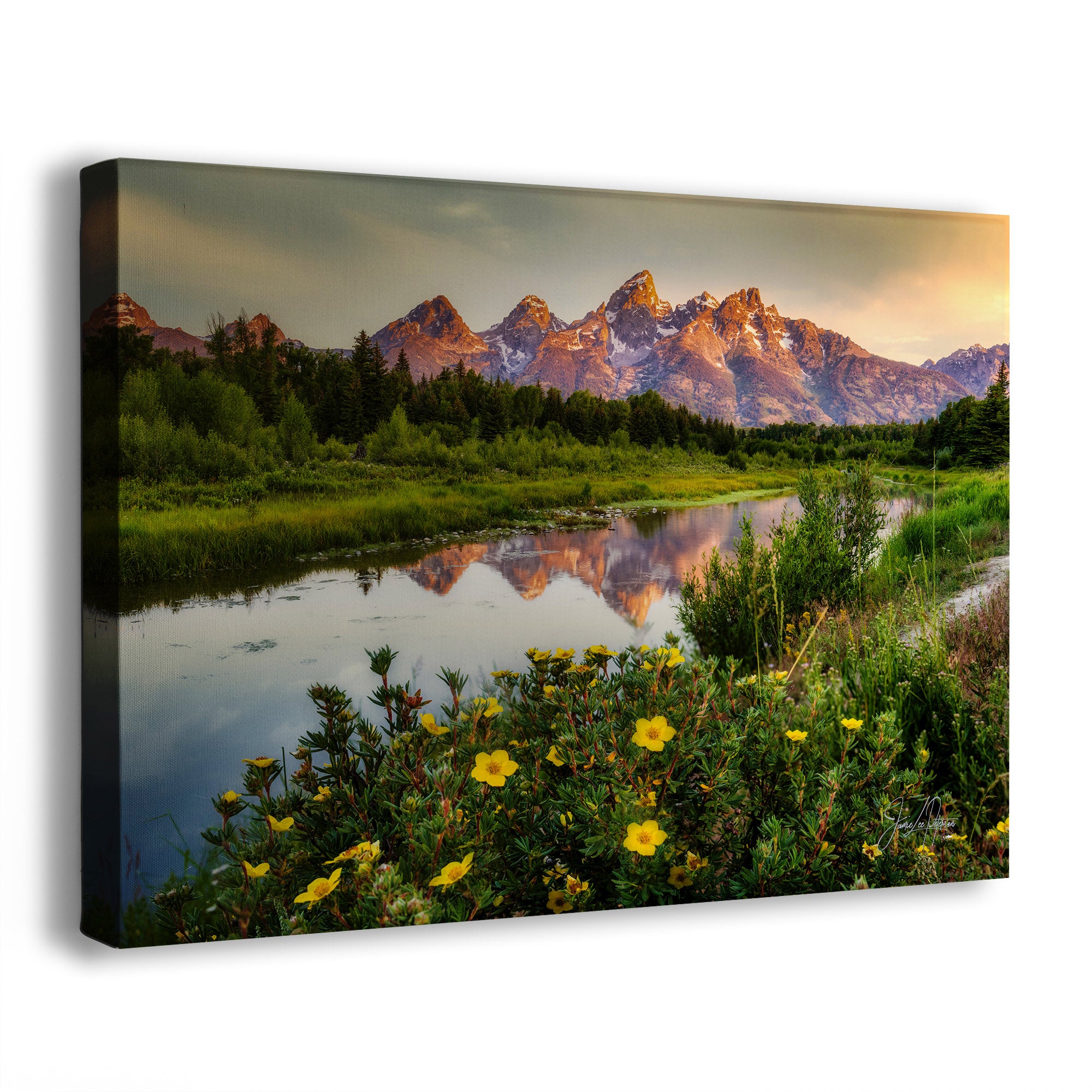 A rectangular canvas wall art print showing the Grand Teton mountain landscape at sunset, with the Snake River reflecting the peaks and wildflowers in the foreground. The canvas is photographed at an angle against a plain white background.