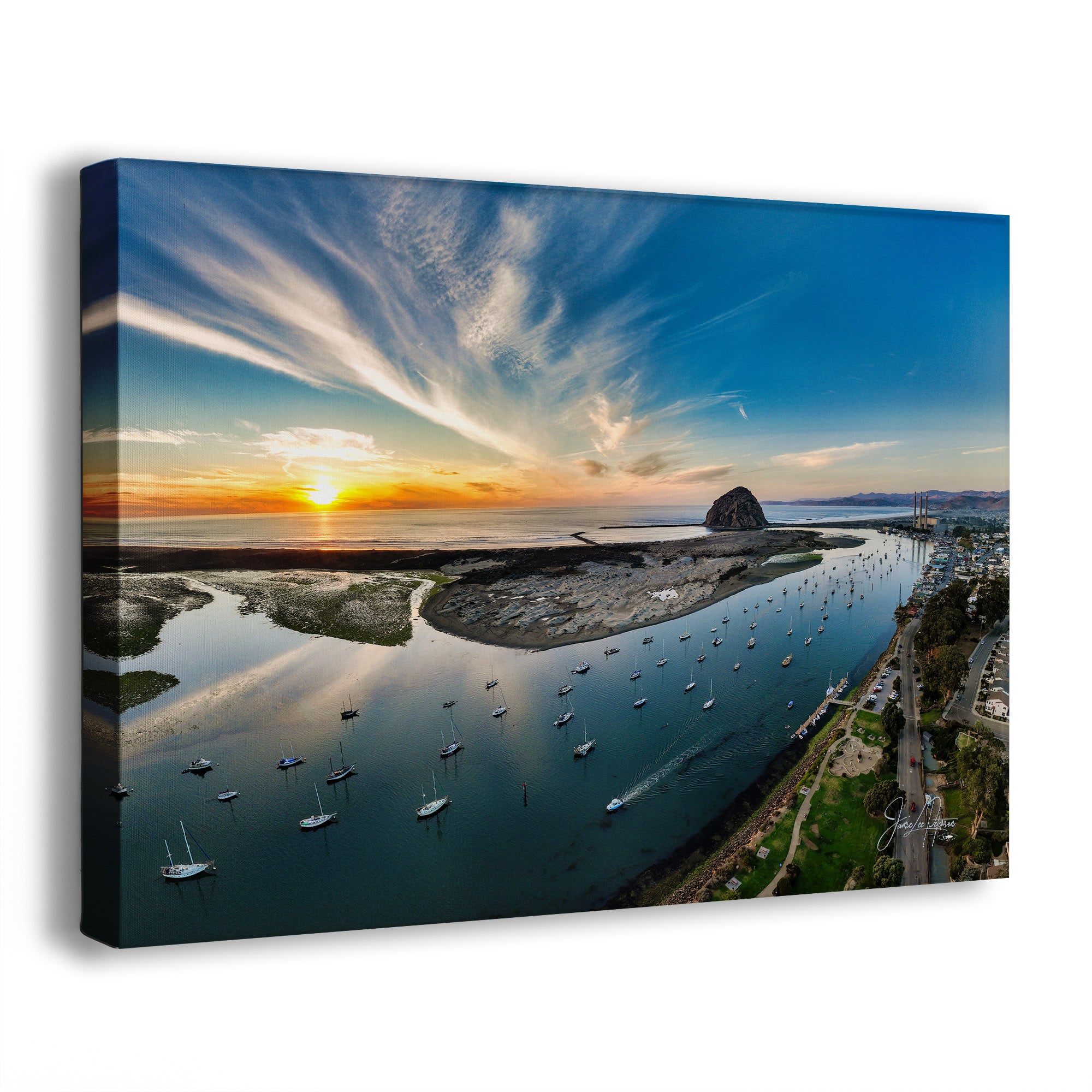 A rectangular canvas wall art print showing an aerial coastal landscape of Morro Bay, California, with a sunset over calm water, boats, marshlands, and a rocky island. The canvas is photographed at a slight angle against a clean white background.