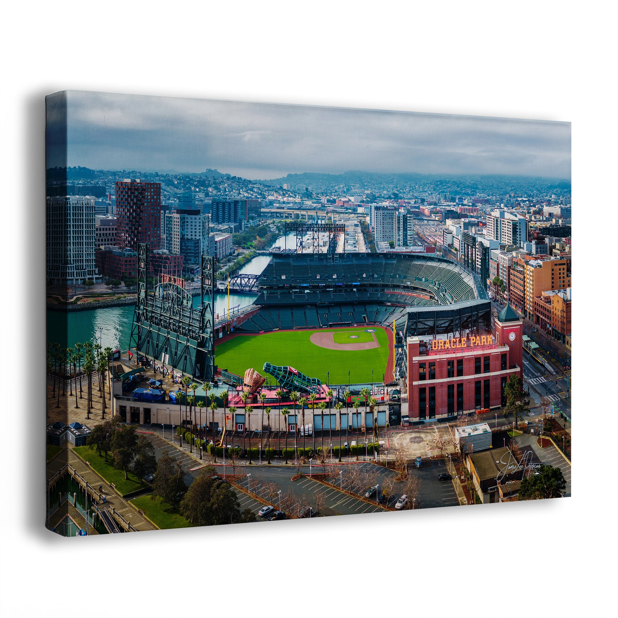An Oracle Park Stadium wall art print showing an aerial view of Oracle Park baseball stadium in San Francisco, with surrounding city buildings, water, and a cloudy sky. The canvas is photographed at an angle against a plain white background.
