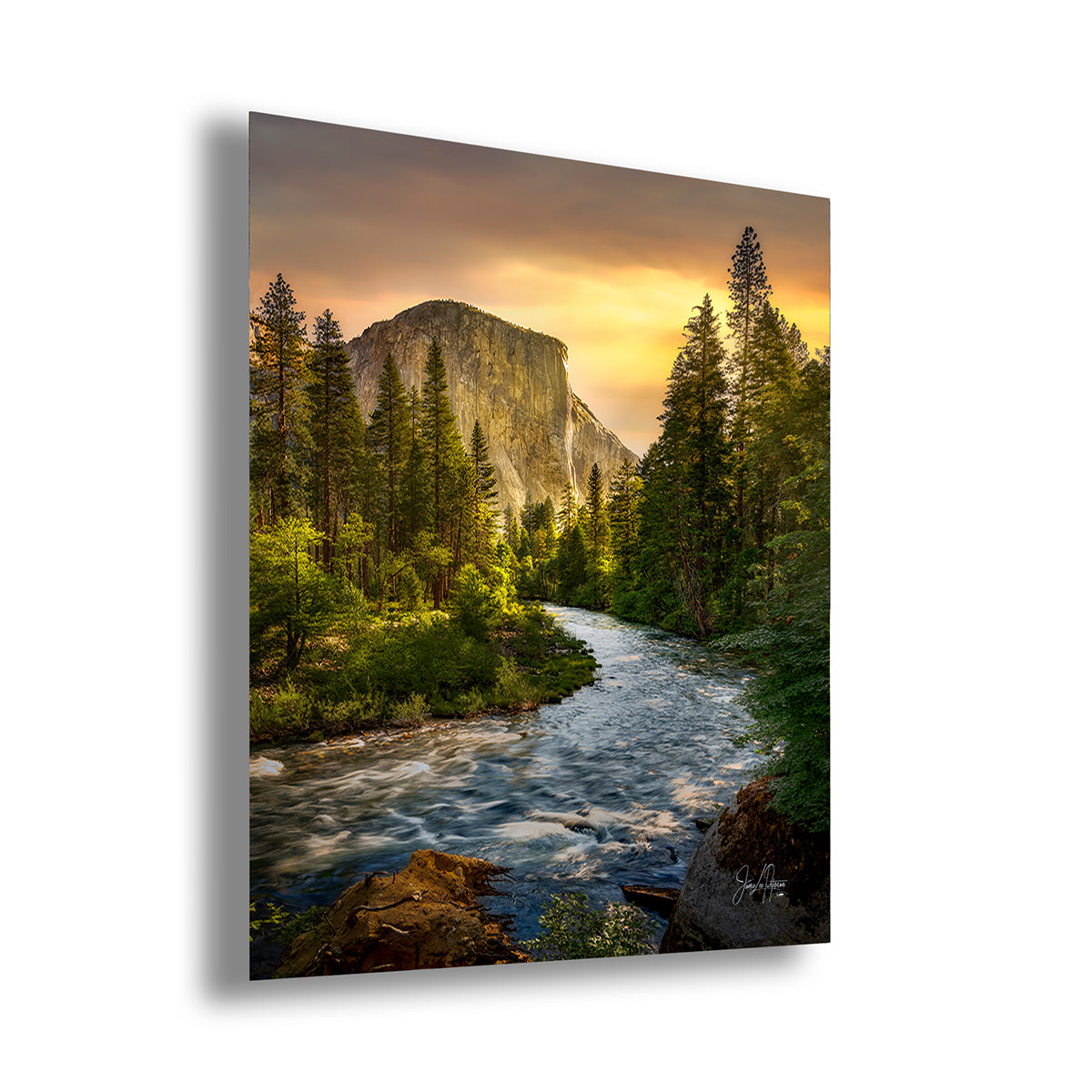 A vertical wall art print depicting a scenic Yosemite landscape of a rushing Merced River flowing through a pine forest toward El Capitan cliff under a warm sunrise sky, shown at a slight angle on a white background.