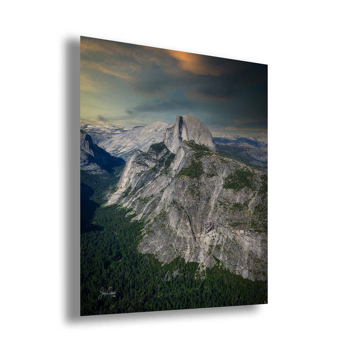 A vertical wall art print of Half Dome in Yosemite depicting a dramatic mountain landscape with a large granite peak, dark forested slopes, and a cloudy sky with warm light near the horizon, shown at a slight angle on a white background.