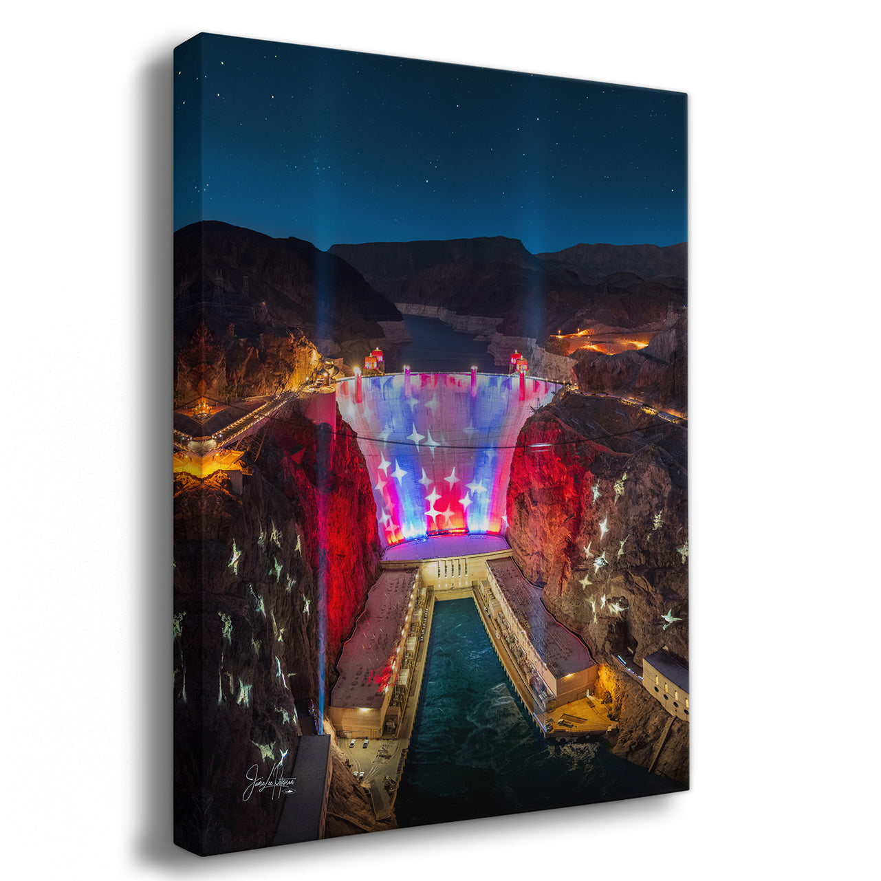 A rectangular wall art print or canvas showing a nighttime Hoover dam scene with colorful illuminated structures, dark cliffs, and a starry blue sky, photographed against a plain white background.