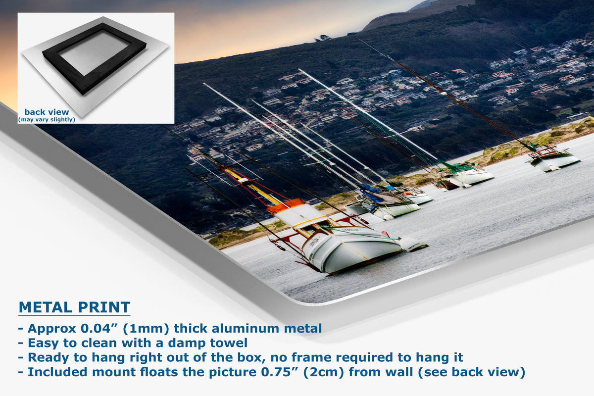 A metal wall art print showing a coastal harbor scene with sailboats, mountains, and buildings, presented at an angle with product text and a small back-view inset on a white background.