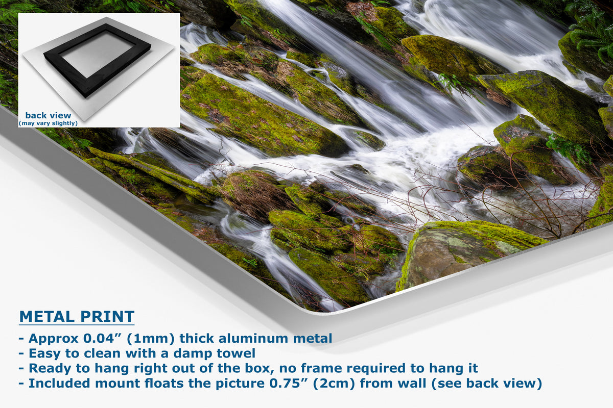 A metal wall art print showing a forest stream flowing over mossy rocks, presented at an angle with product details and text on a white background. The text highlights the aluminum metal finish and mounting features.