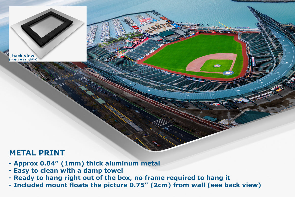 A corner view of an aluminum metal wall art print showing an aerial view of a baseball stadium, presented at an angle with a small back-view inset and product text on a white background. The print appears to be a metal print with a black frame mount.