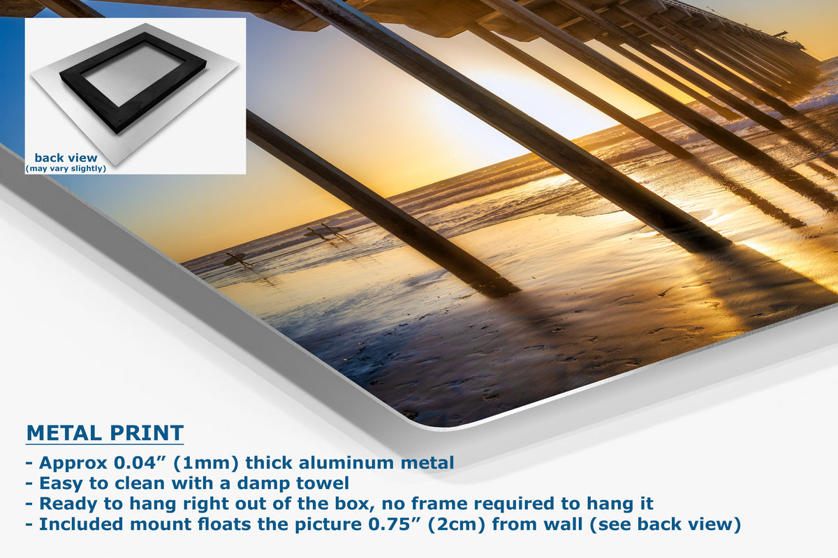 A metal print wall art product shown at an angle on a white background, with a small inset showing the back view and text describing the aluminum finish and mounting details. The artwork depicts a beach scene at sunset with wooden posts overhead.