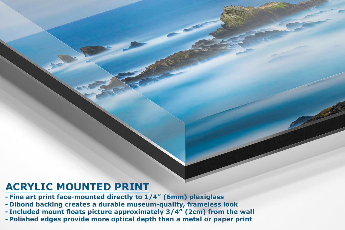 Acrylic mounted art print of a coastal landscape with blue water, white surf, and rocky cliffs, shown at an angle with product text overlay on a white background.