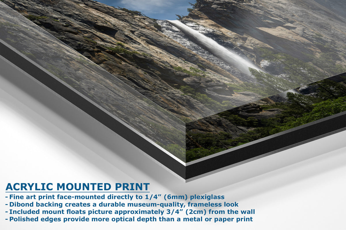 A corner view of an acrylic mounted art print of a mountain landscape with a waterfall, shown at an angle with text detailing the mounting features and dimensions.