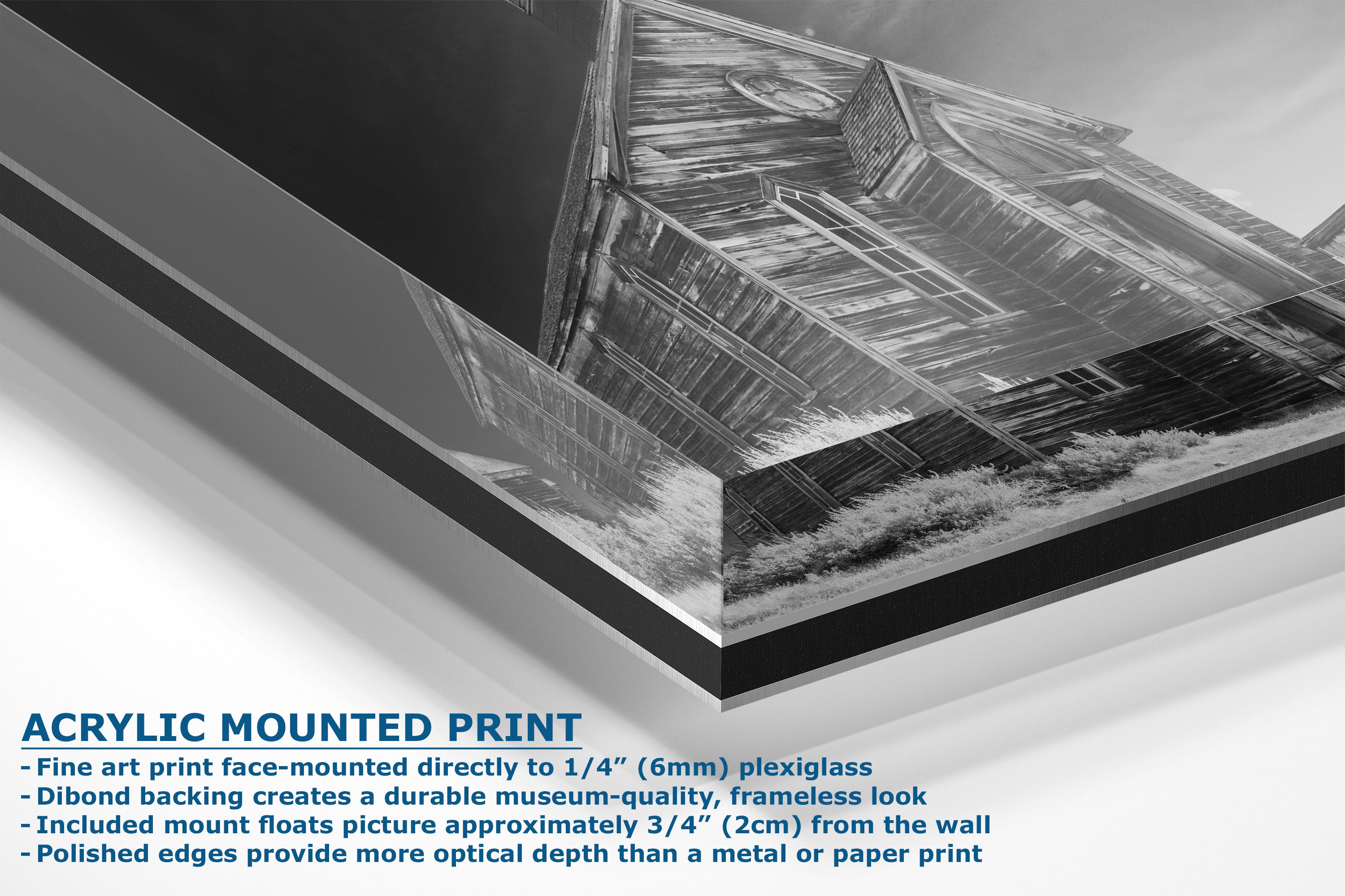 A corner view of an acrylic mounted art print showing a black and white photograph of a rustic wooden barn, with descriptive text on the bottom left detailing the mounting features.