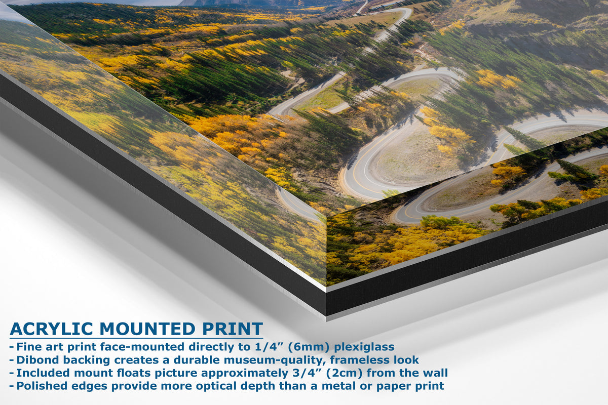 A corner view of an acrylic mounted art print of a winding road through a forested mountain landscape, shown at an angle with descriptive text on a white background.