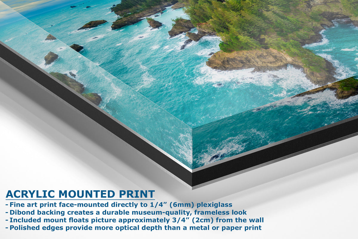 A corner view of an acrylic-mounted art print of a coastal landscape with turquoise water, green cliffs, and white surf, shown at an angle with product text on a white background.