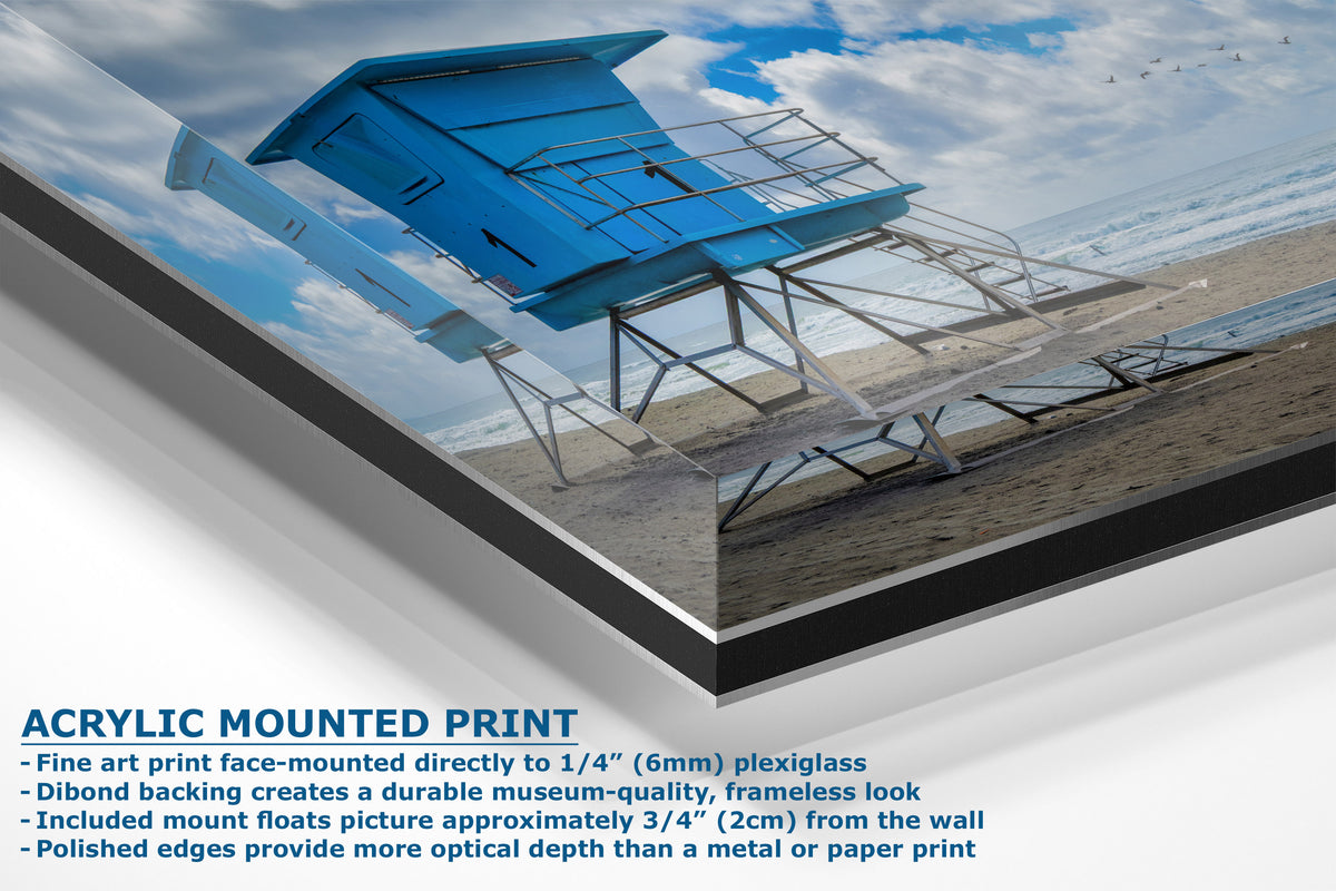 Acrylic mounted art print featuring a beach scene with a blue lifeguard tower, shown at an angle with descriptive text on a white background.