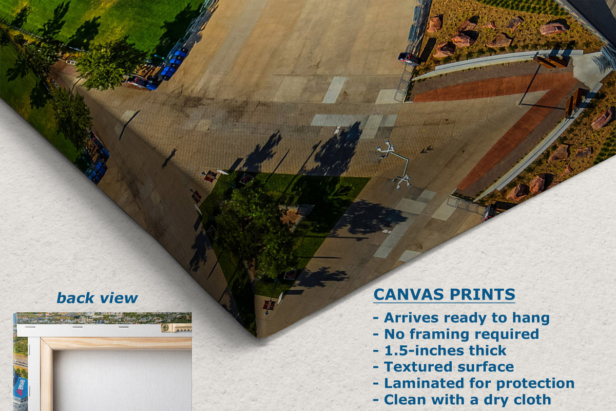A corner view of a canvas wall art print shown at an angle on a light textured background, displaying an aerial view of a paved plaza with trees and landscaping. The image includes marketing text for canvas prints and a small inset labeled back view.