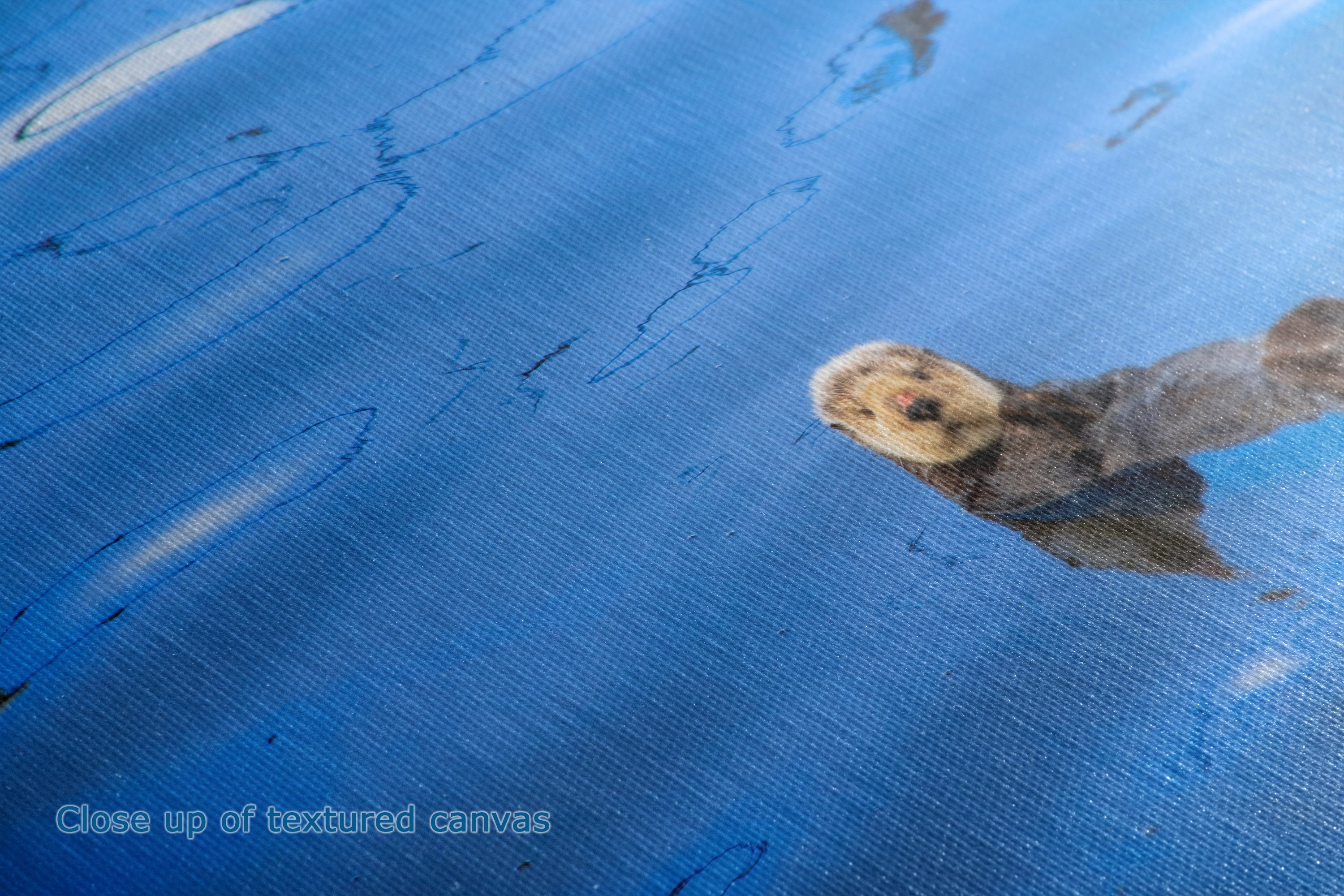 Close-up of a blue textured canvas surface with a small printed or painted patch near the upper right and faint watermark text in the lower left.
