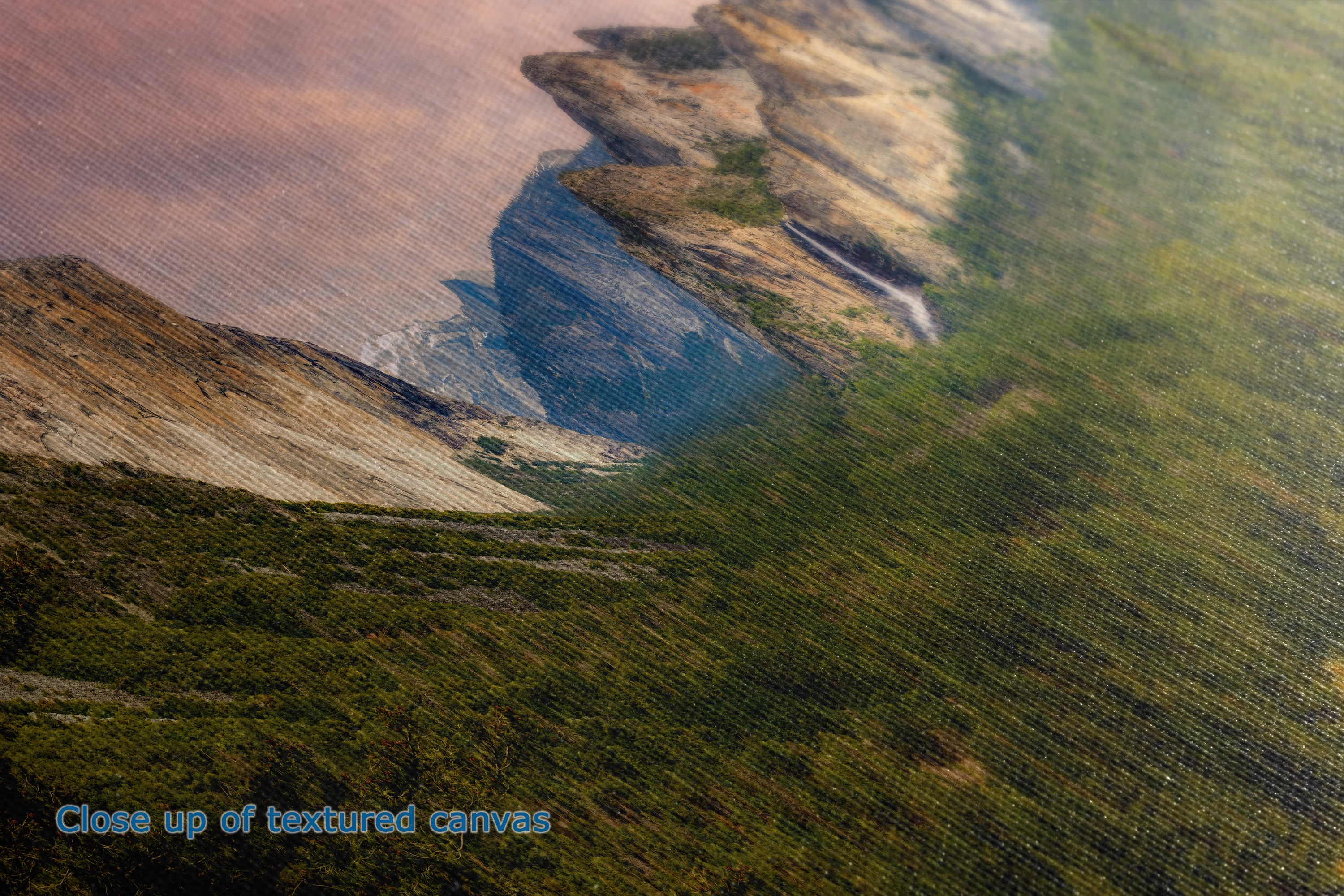 Close-up of a textured canvas print showing a landscape scene with green hills, a blue cliff, and warm brown sky, with the text 'Close up of textured canvases' in the lower left corner.