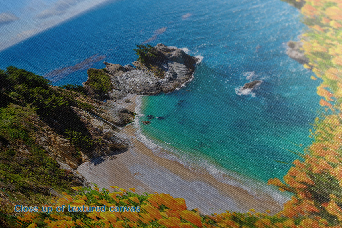 Close-up of a textured canvas print depicting a scenic coastal landscape with turquoise ocean water, rocky shoreline, sandy beach, and autumn foliage.