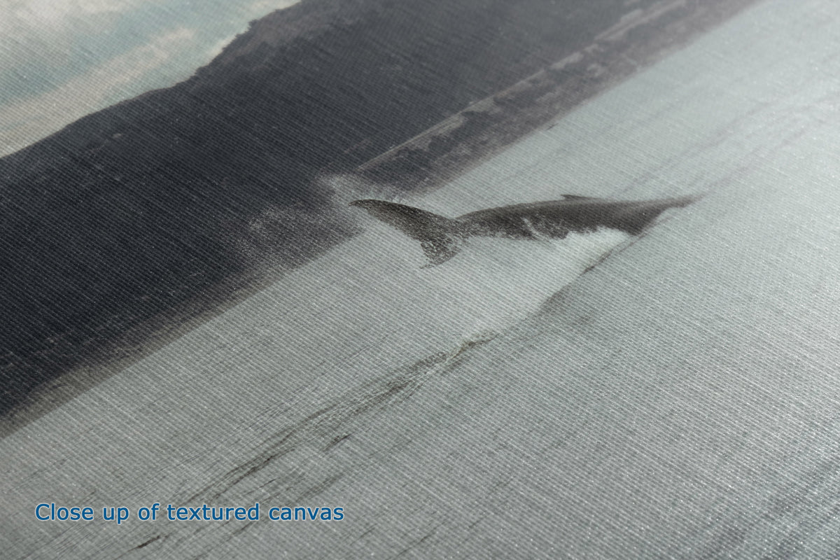 A close-up of a textured canvas print depicting a dramatic coastal scene with a dark rocky shoreline and a large gray whale breaching the water, with blue text in the corner reading 'Close up of textured canvas'.