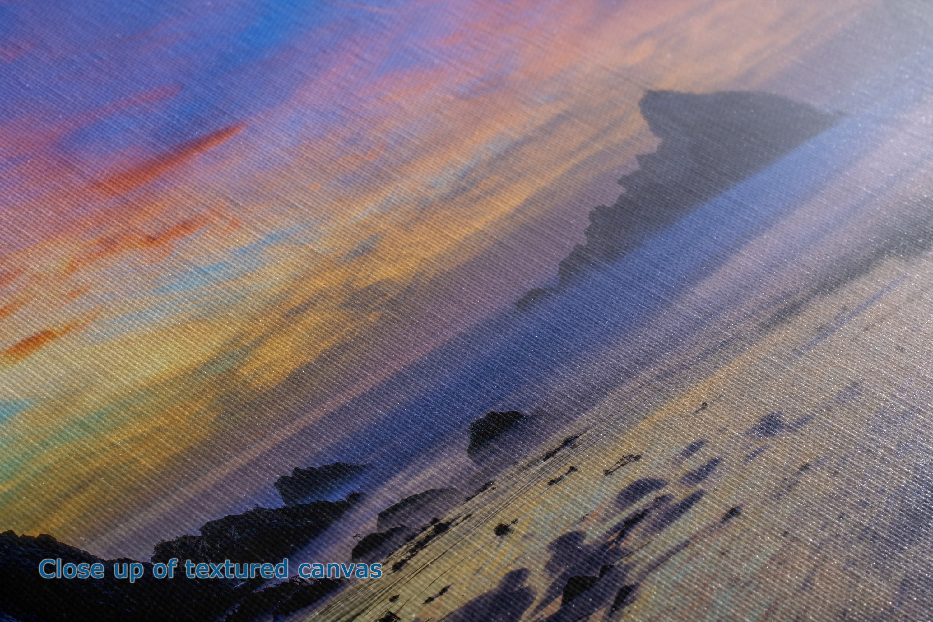 Close-up of a textured canvas painting depicting a coastal sunset scene with blue, purple, orange, and yellow tones]. Text in the lower left reads 'Close up of textured canvas.
