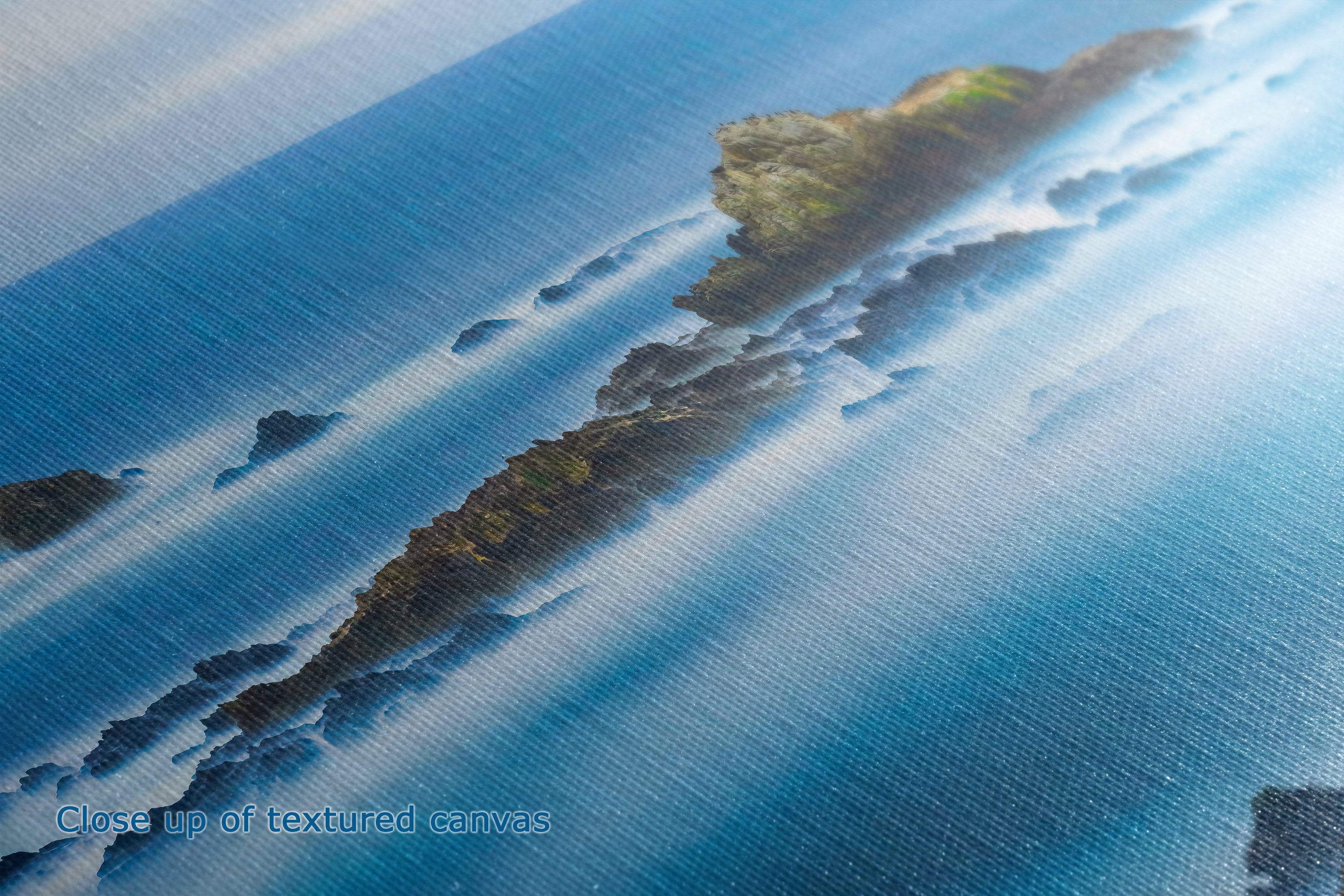 Close-up of a textured canvas print depicting a coastal landscape with a narrow rocky island surrounded by deep blue water and bright sunlight.