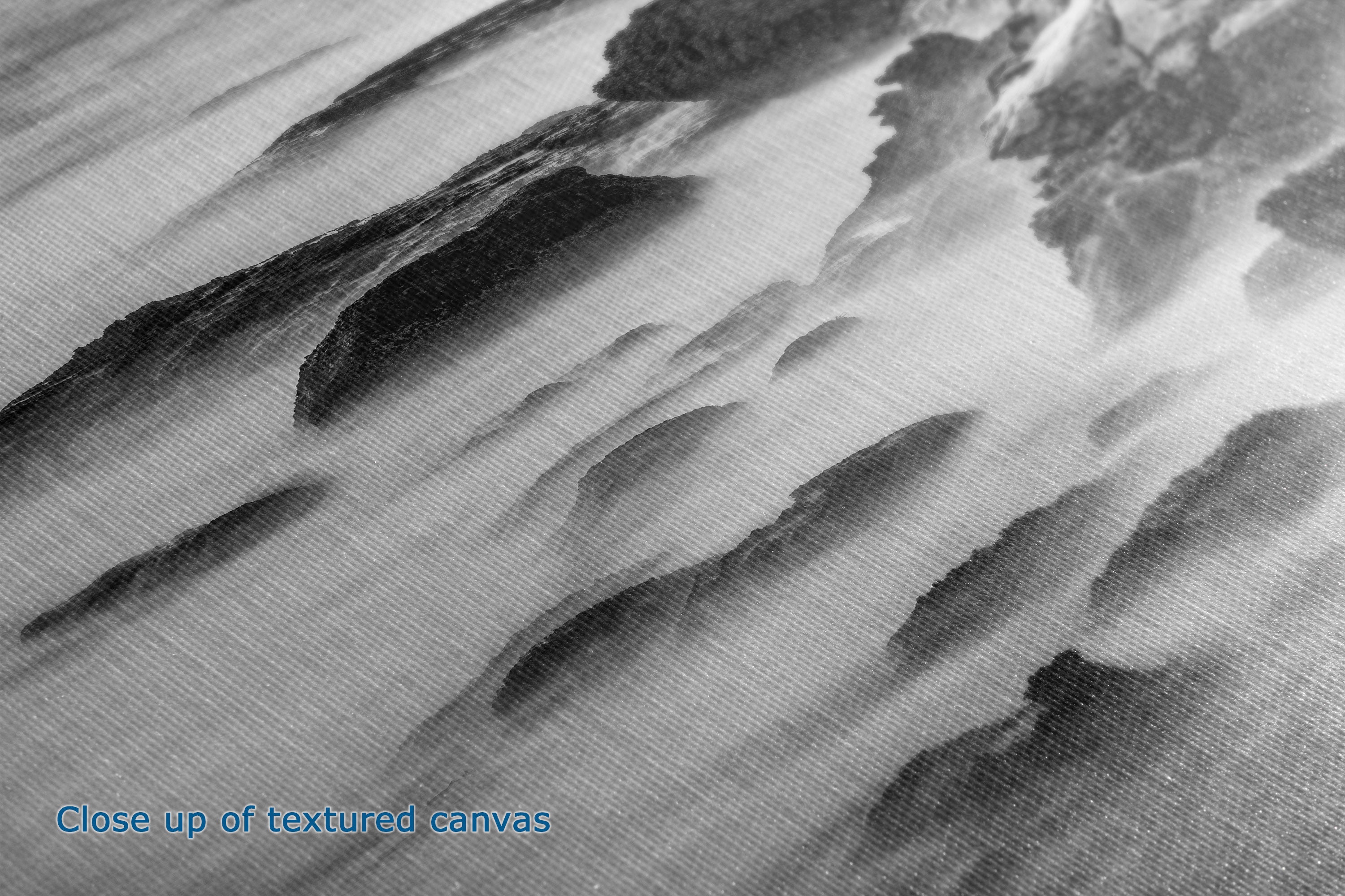 Close-up of a textured canvas print featuring an abstract black and white landscape design with layered mountain-like shapes and misty clouds. Blue text in the lower-left corner reads 'Close up of textured canvas'.