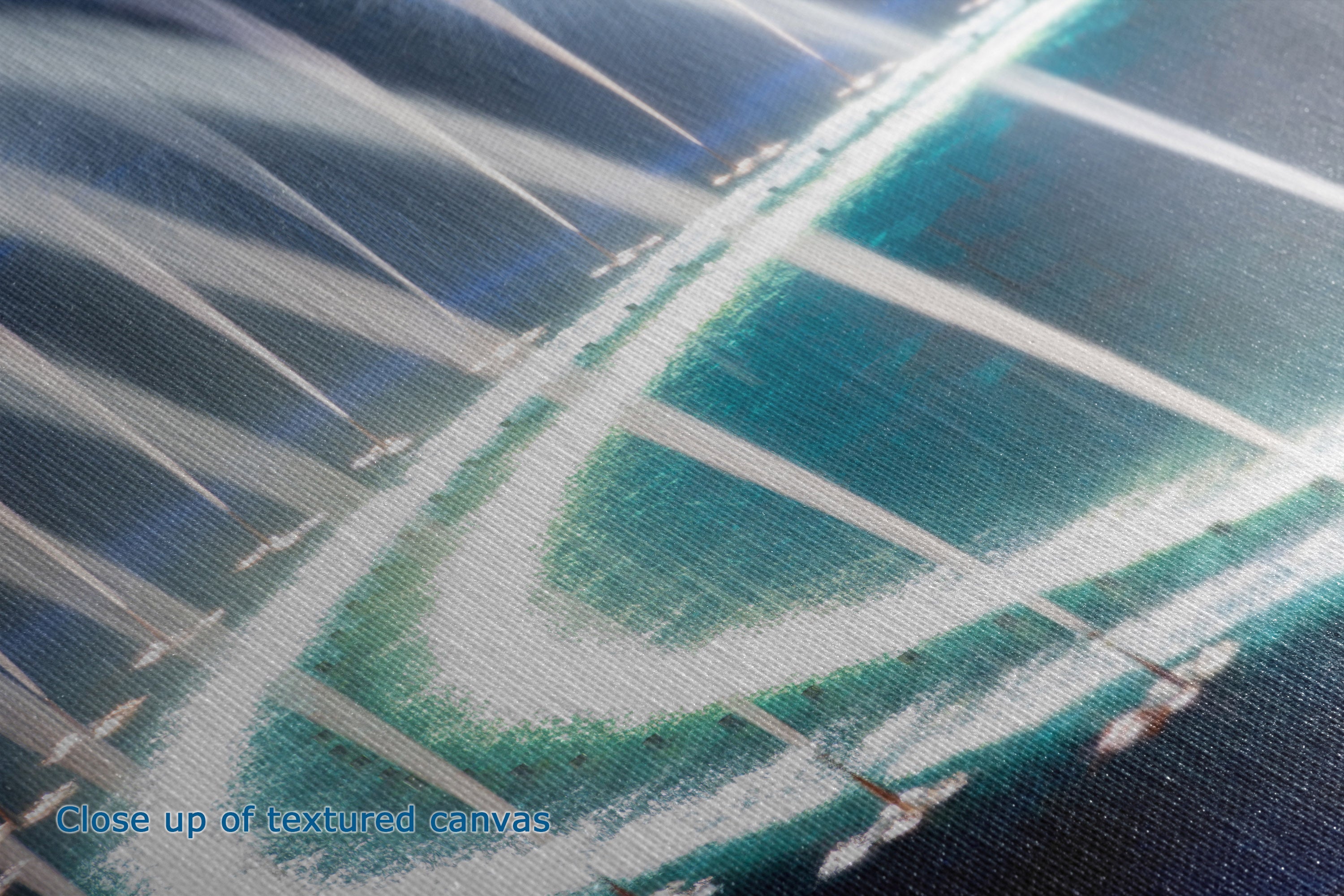 Close-up view of the detail and texture of a canvas print showing an abstract coastal scene with turquoise water, white surf, and dark blue shoreline. Blue text in the lower-left corner reads 'Close up of textured canvas.