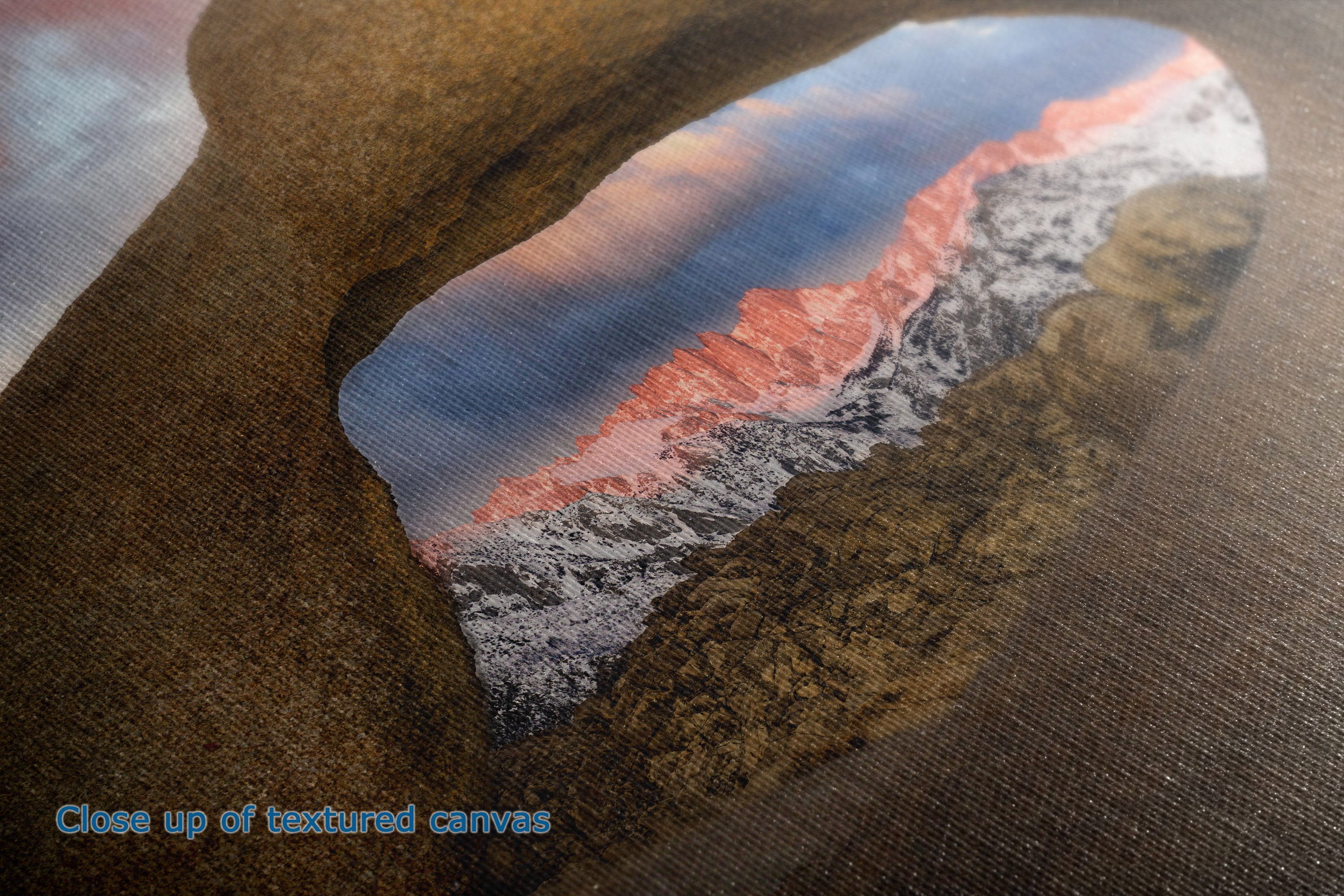 Close-up of a textured canvas print showing a mountain landscape scene framed by a dark rock arch, with the text 'Close up of textured canvas' in the lower left corner.