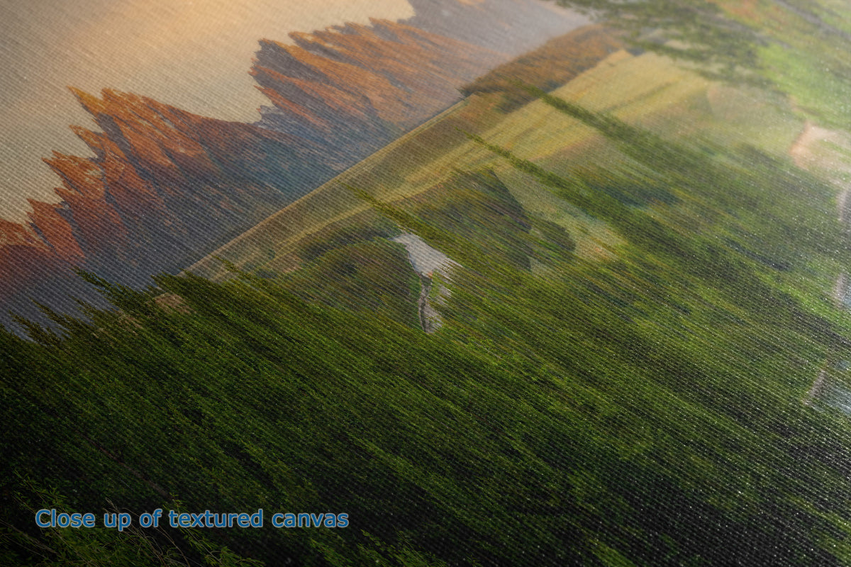 Close-up of a textured canvas print showing a landscape painting with green fields, brown hills, and a warm sunset sky. Blue text in the lower-left corner reads 'Close up of textured canvas'.