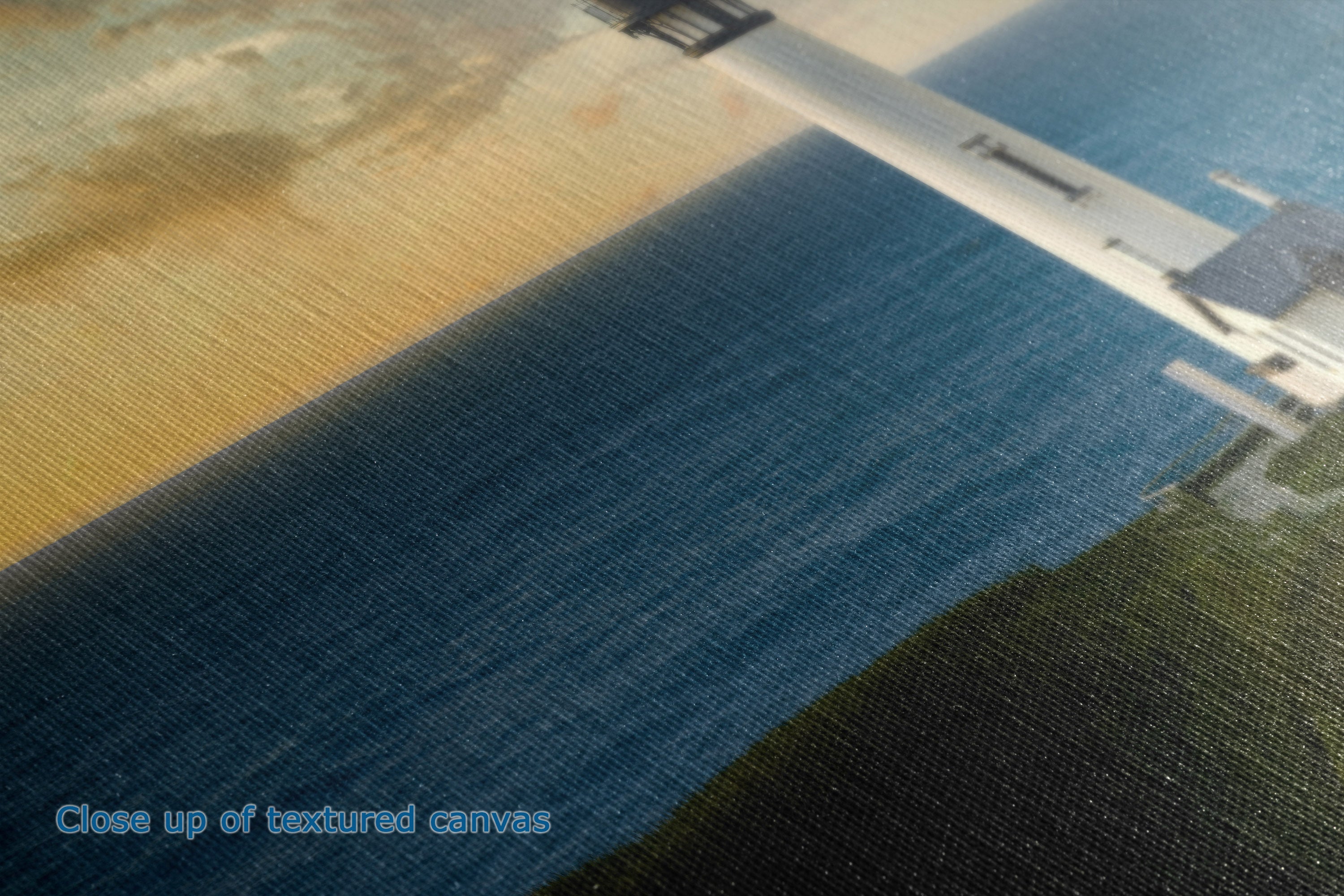 Close-up of a textured canvas print showing a coastal scene with deep blue water, sandy beige shore, dark green land, and a white pier, with the text 'Close up of textured canvases' in the lower left corner.