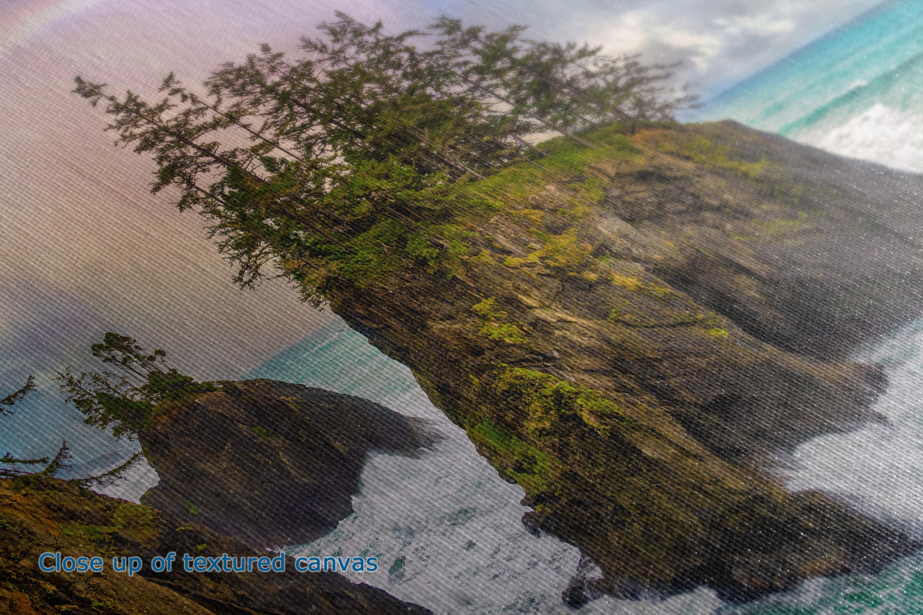 Close-up of a textured canvas print depicting a dramatic coastal cliff with green trees growing out of the rock, overlooking turquoise ocean water with white waves. Blue text in the lower-left corner reads 'Close up of textured canvas'.