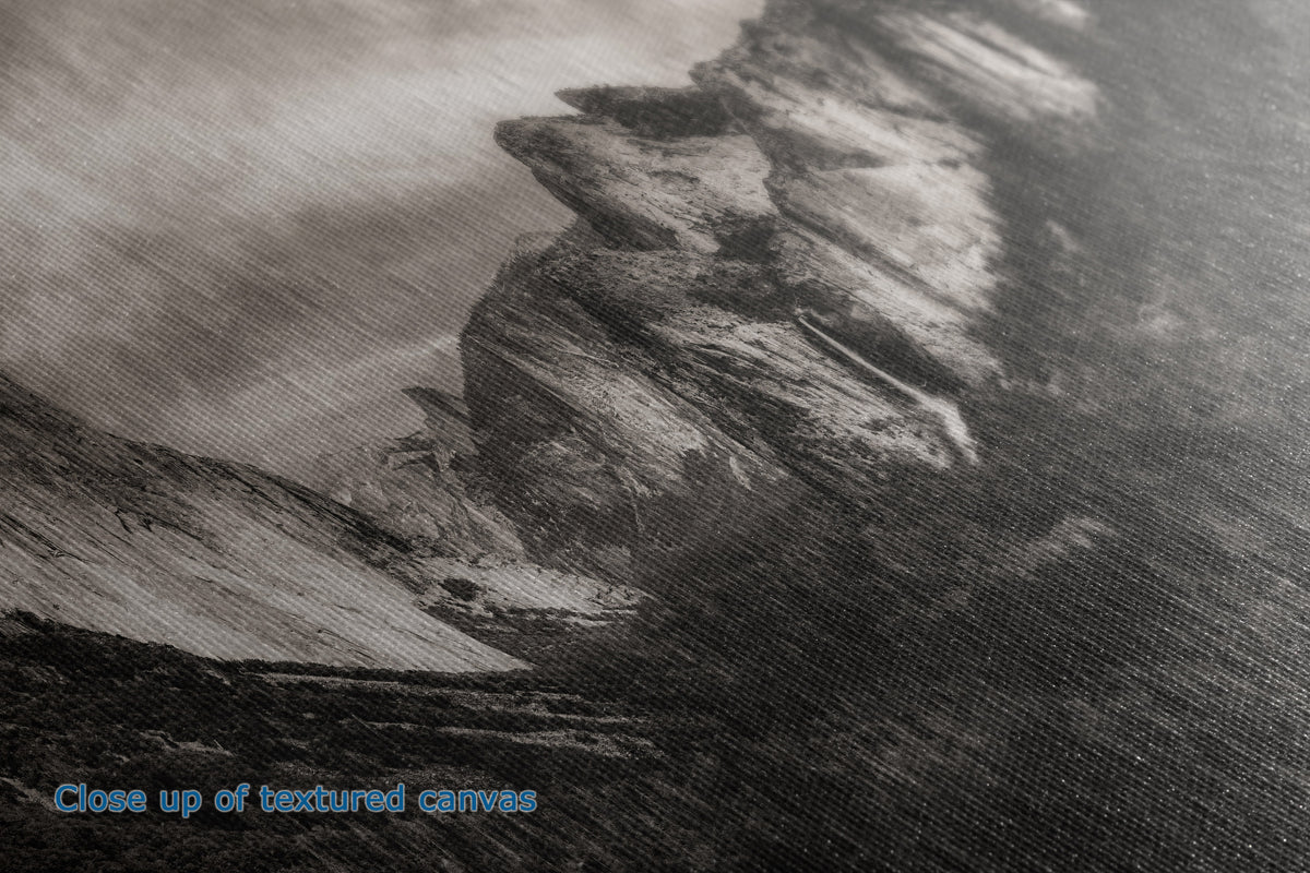 Close-up of a textured canvas print depicting a dramatic rocky cliffside or mountain slope in grayscale tones, with blue text in the lower-left corner reading 'Close up of textured canvas'.