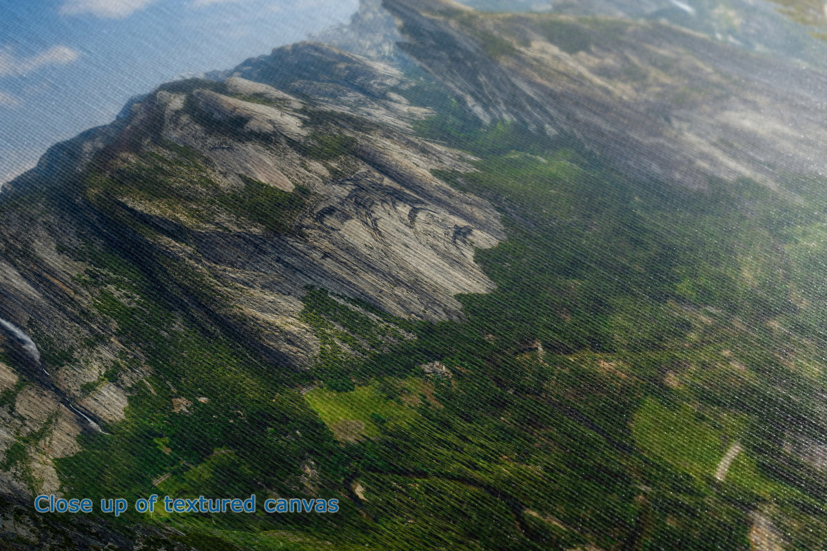 Close-up of the detail and texture of a canvas print depicting a rugged mountain landscape with green forests and rocky cliffs under a blue sky.