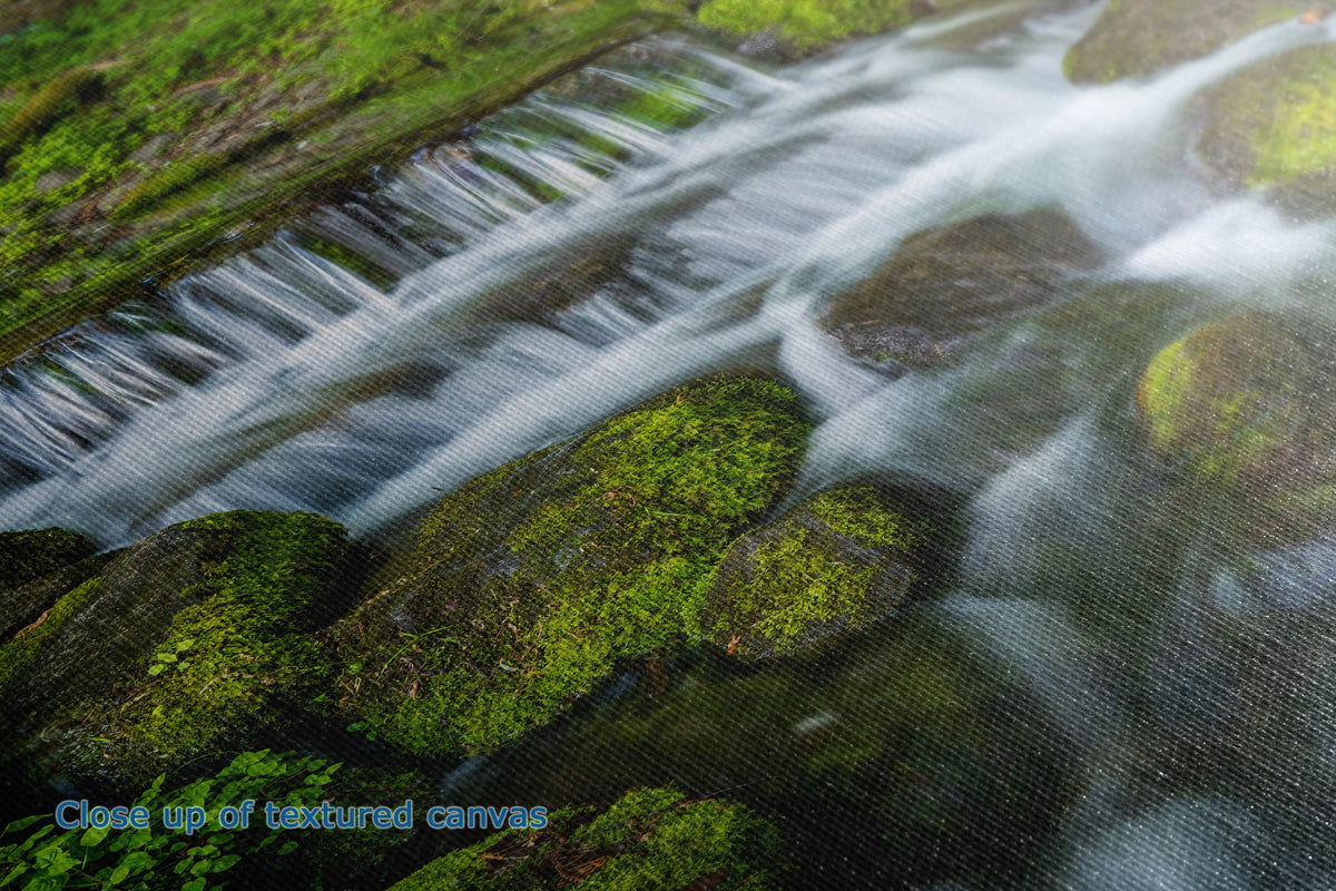 Close-up of a textured canvas print depicting a scenic landscape of a small waterfall flowing over mossy green rocks.