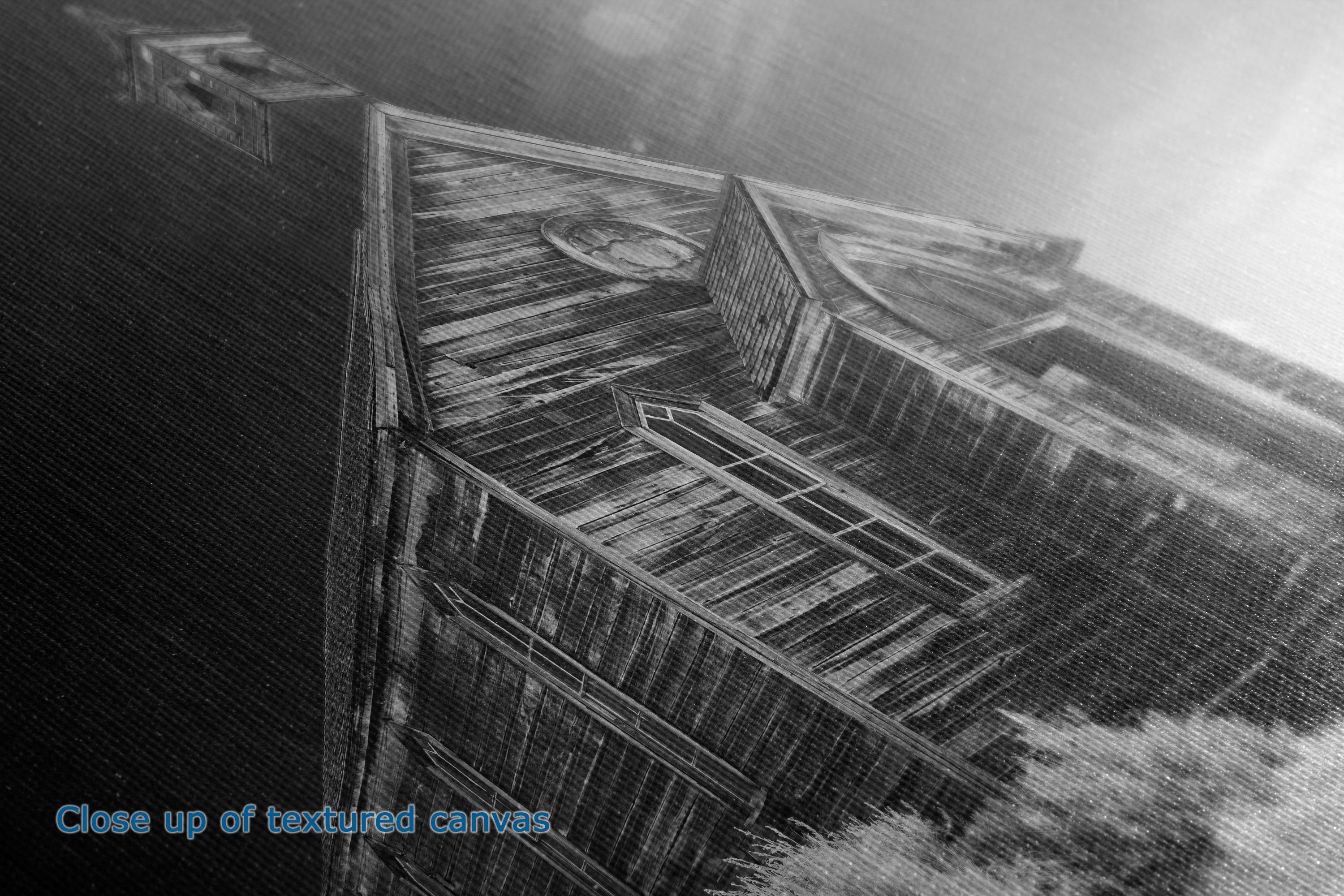 Black and white close-up of the texture and detail of a canvas print showing a weathered wooden structure with a window, showing fine canvas weave details.
