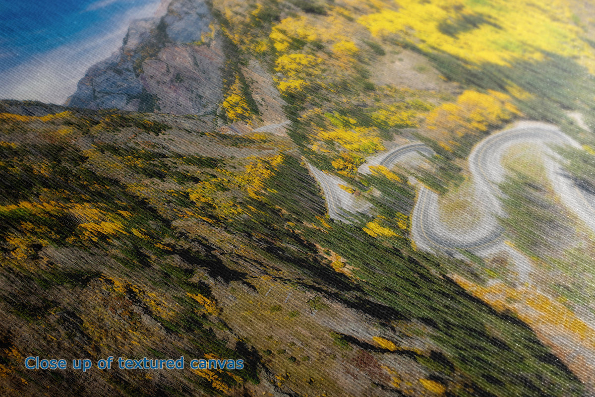 Close-up of the detail and texture of a canvas painting depicting a winding mountain road through yellow and green hills under a blue sky.