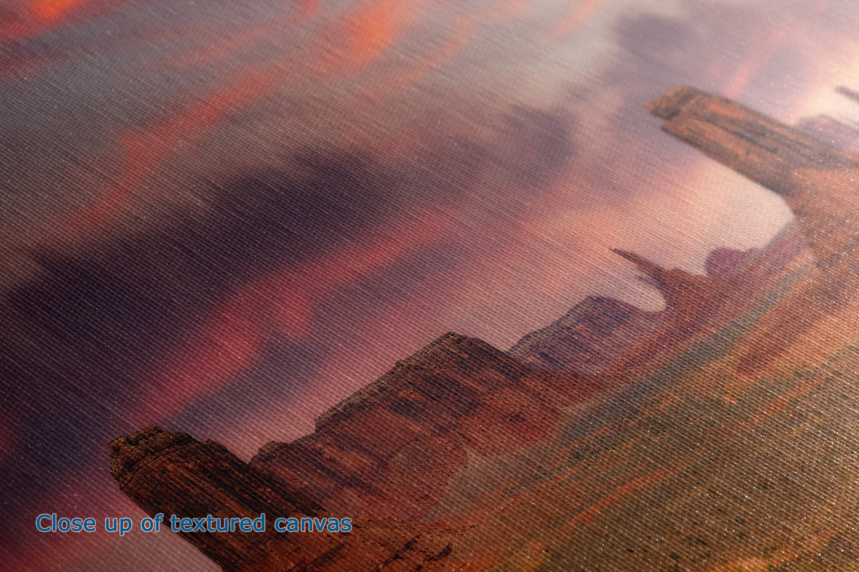 Close-up of a textured canvas print depicting a desert landscape with red and orange rock formations under a cloudy sky.