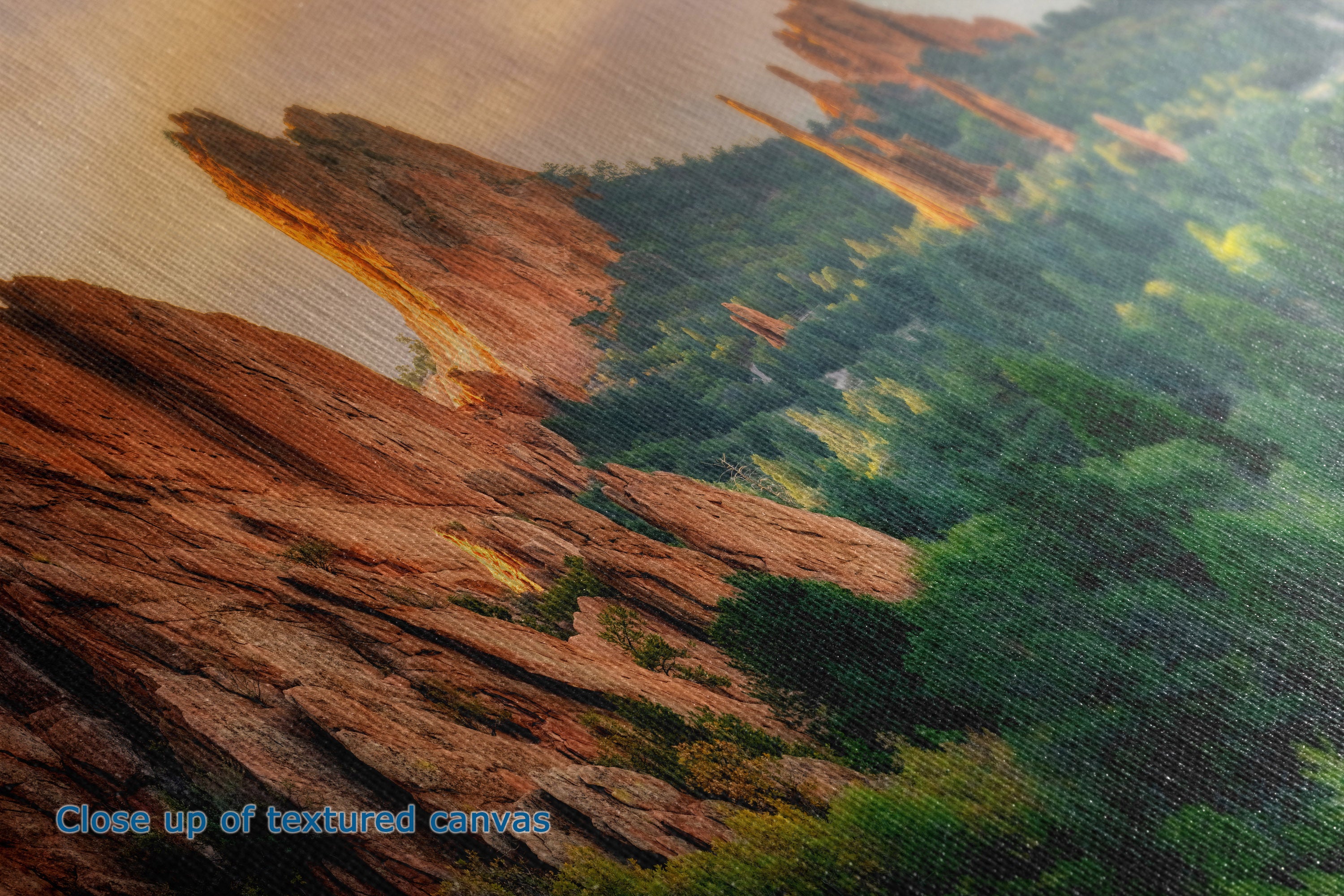 Close-up of the detail and texture of a canvas print depicting a scenic landscape with reddish-brown rock formations and green forest under a warm sky.