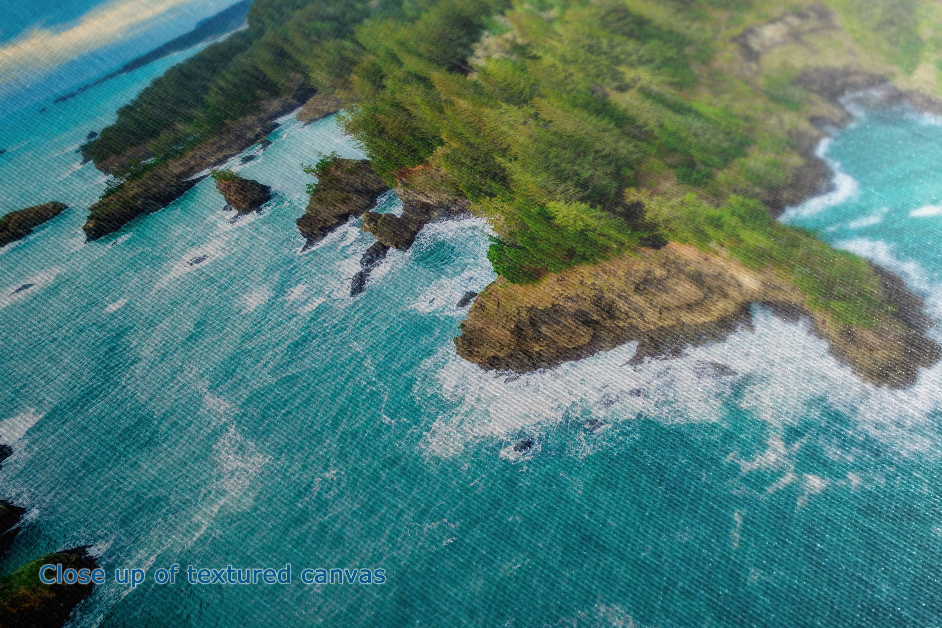 Close-up of a textured canvas print depicting a tropical coastline with turquoise ocean water, white surf, and lush green cliffs.