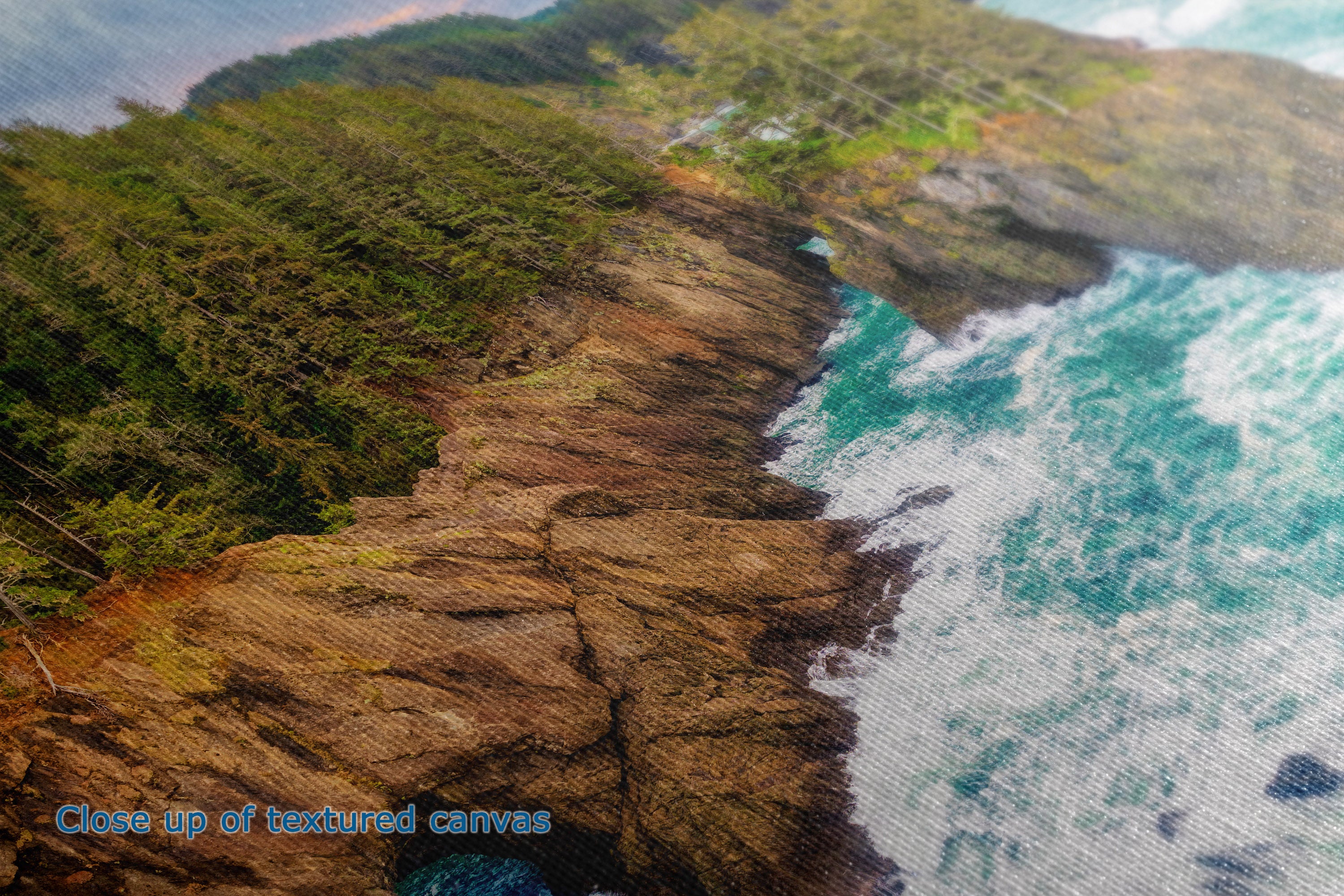 Close-up of a textured canvas print depicting a rugged rocky coastline with green forested cliffs and turquoise ocean waves crashing, with blue text in the lower-left corner reading 'Close up of textured canvas'.