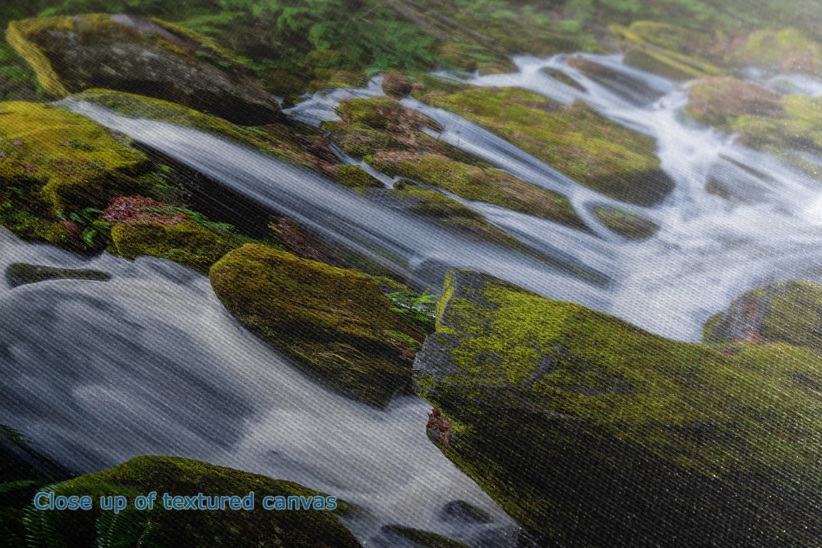 Close-up of a textured canvas print depicting a scenic landscape with mossy rocks and flowing water, with the text 'Close up of textured canvas' in the bottom-left corner.